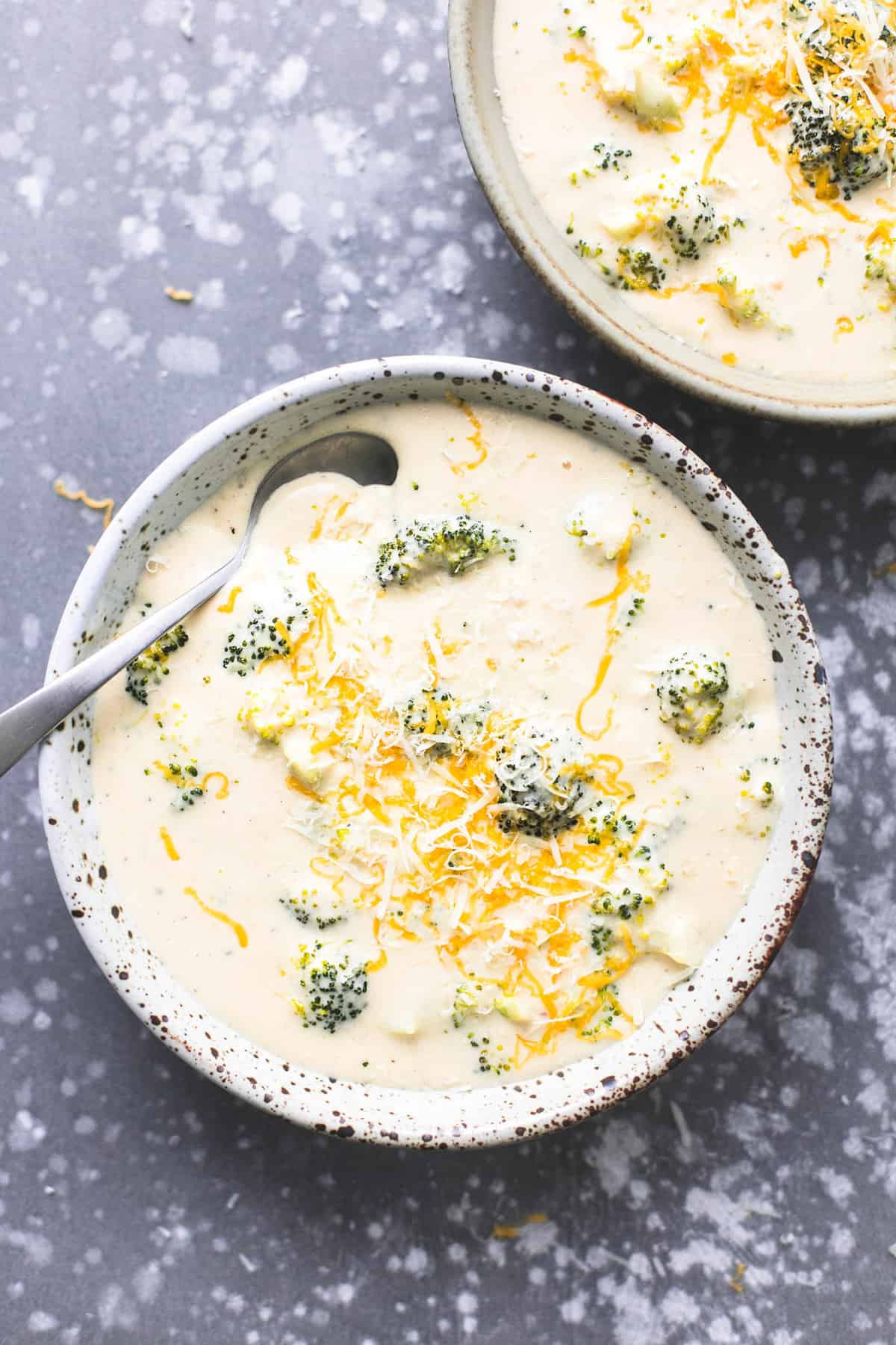top view of broccoli cheese soup with a spoon in a bowl with another bowl of soup on the side.