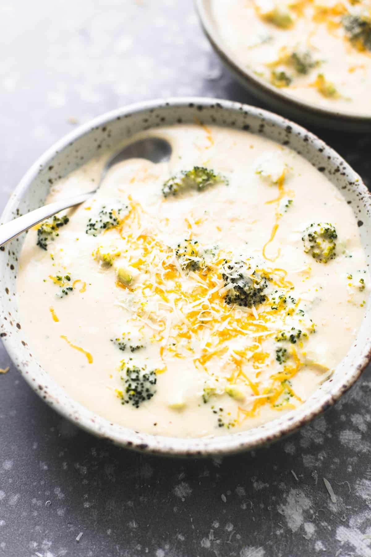 broccoli cheese soup with a spoon in a bowl with another bowl of soup in the background.