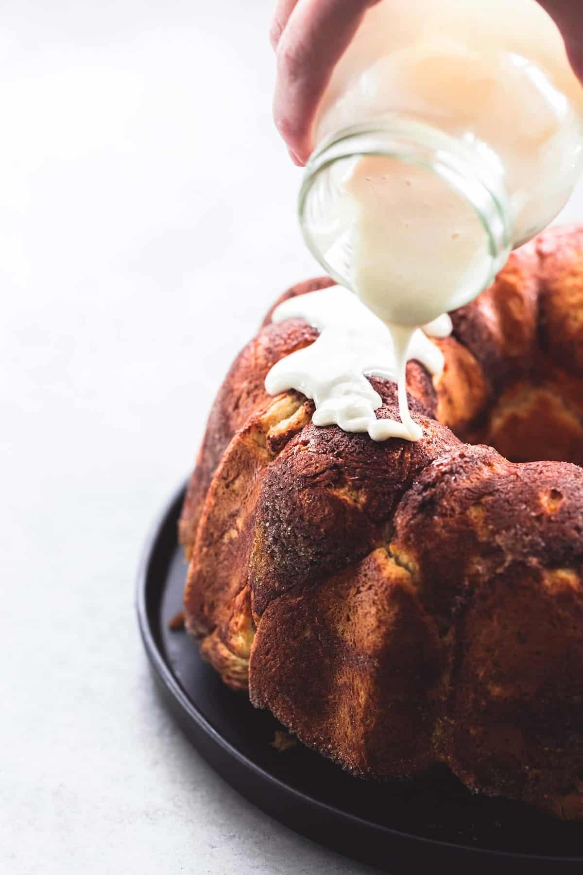 cinnamon swirl monkey bread with glaze being poured on top from a jar.