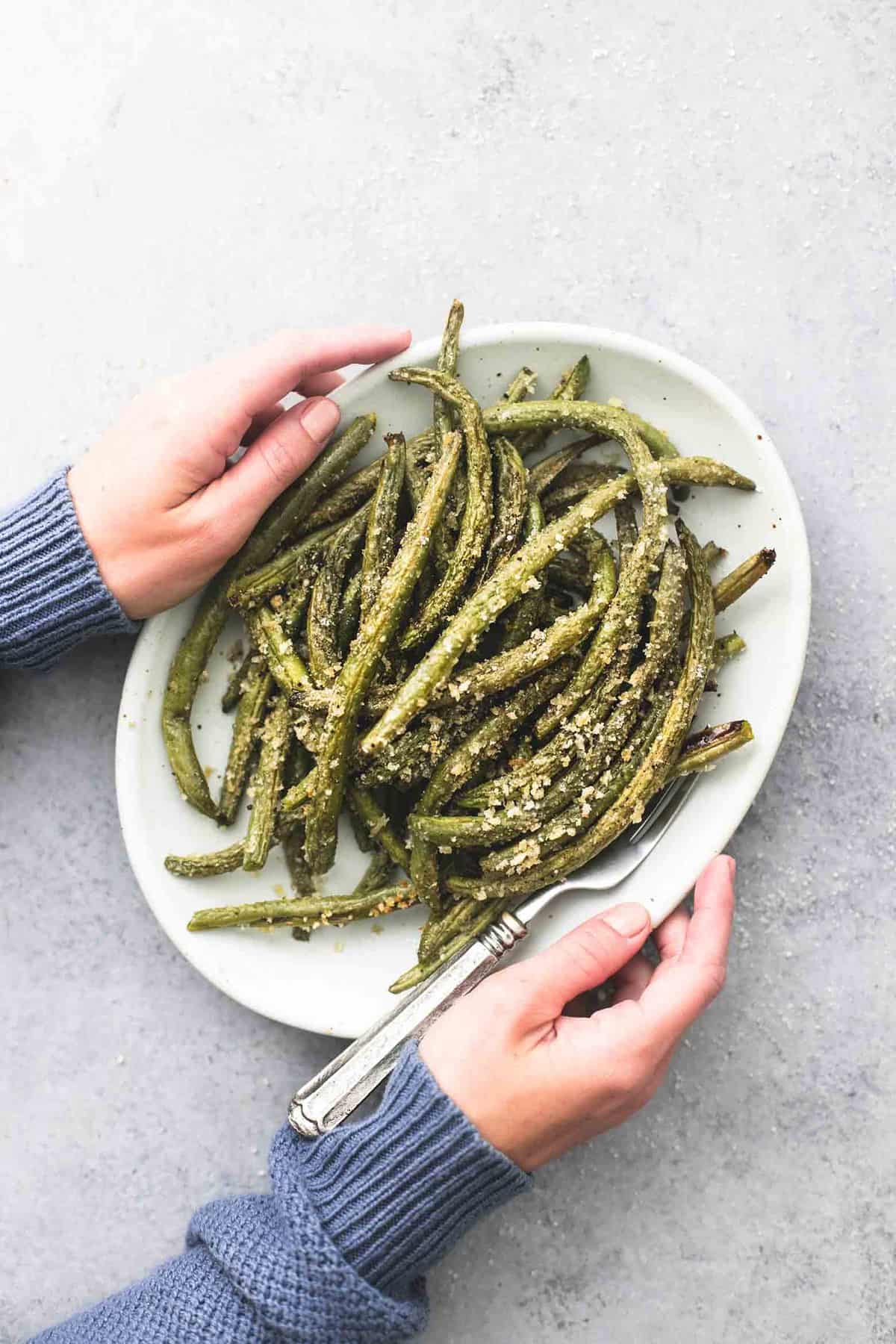 top view of a pair of hands holding a plate with a fork and crispy parmesan green beans on it.