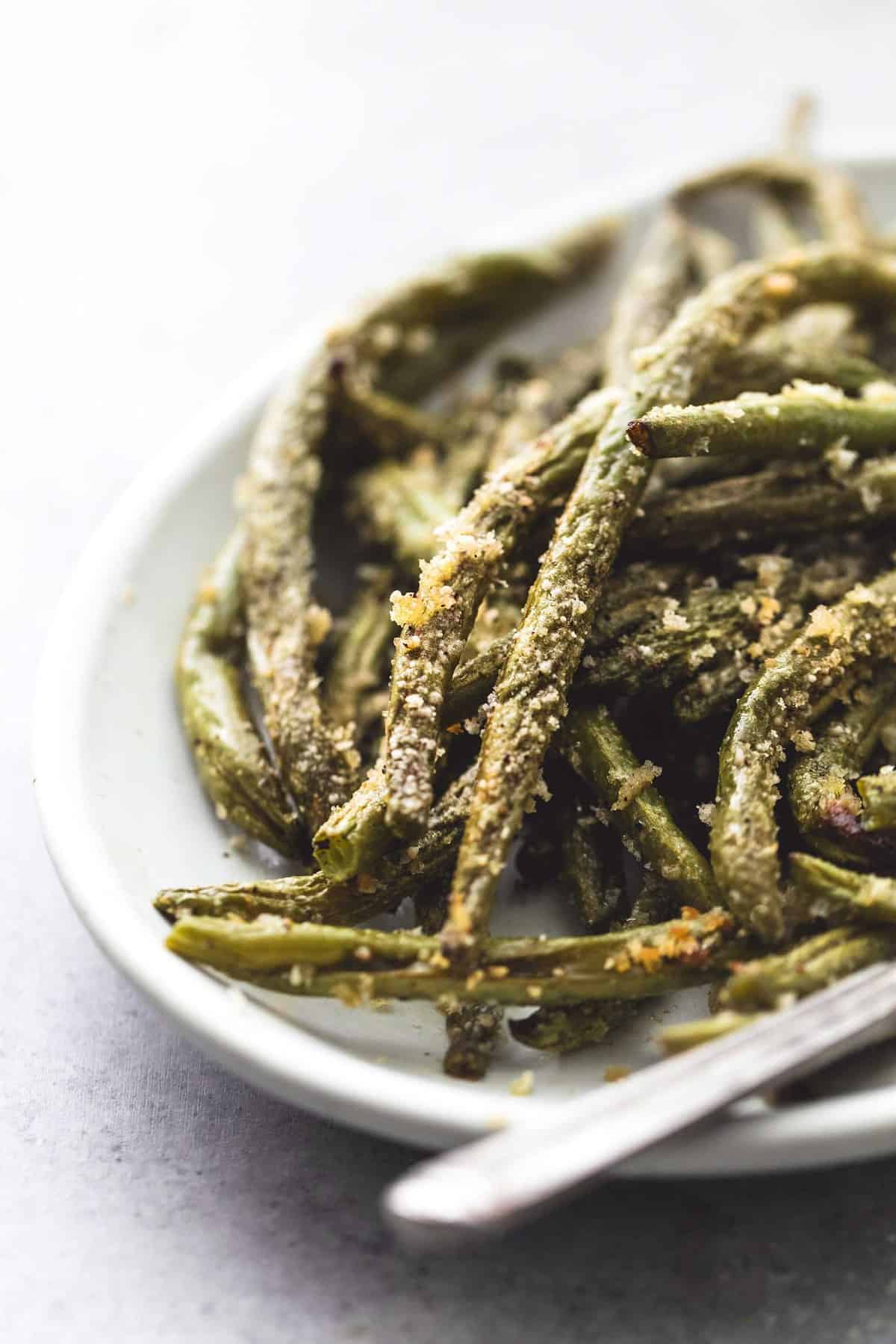 close up of crispy parmesan green beans and a fork on a plate.