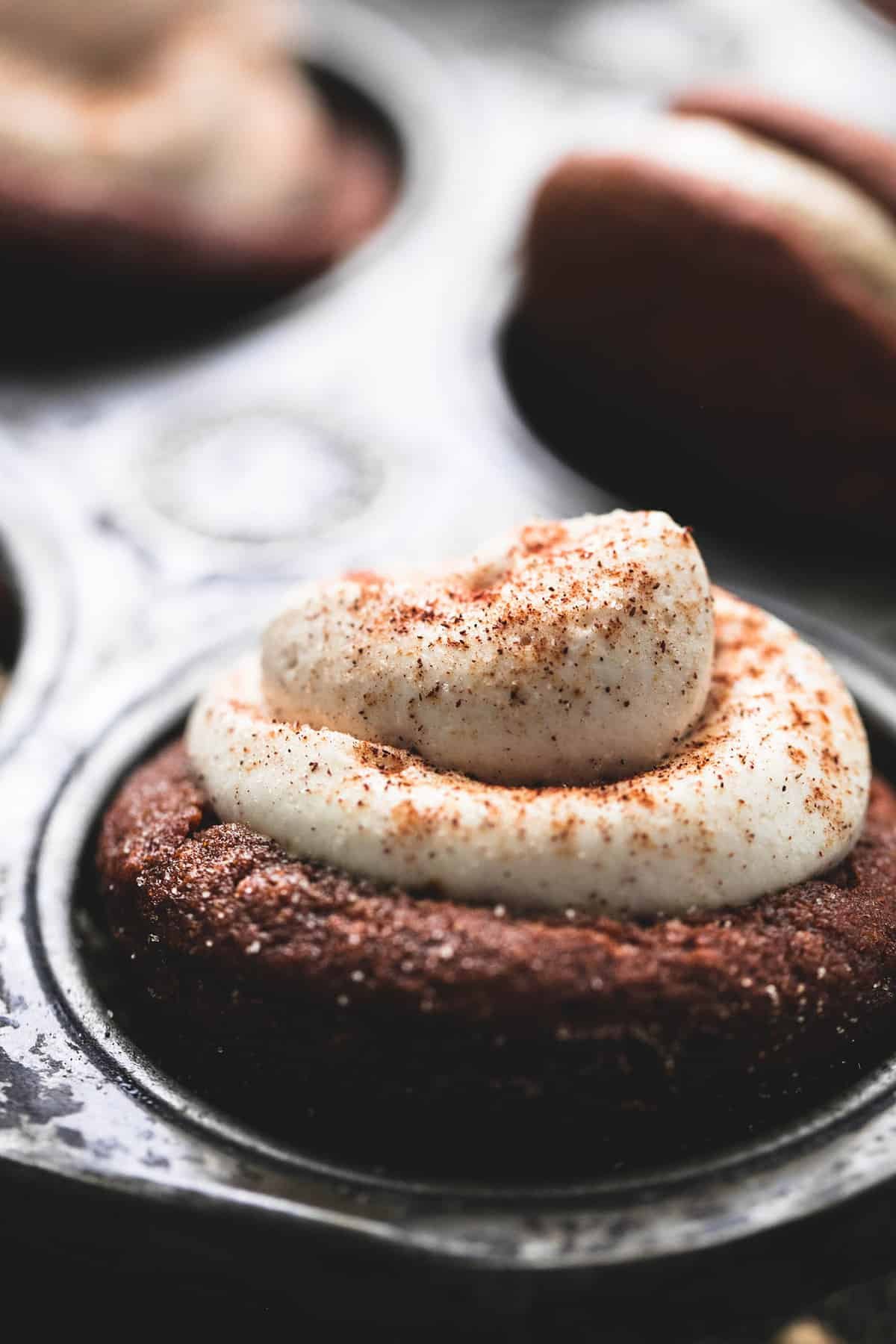 close up of a gingerbread cheesecake cup with more cups and whoopie pies with caramel frosting faded in the background all in a muffin tin.