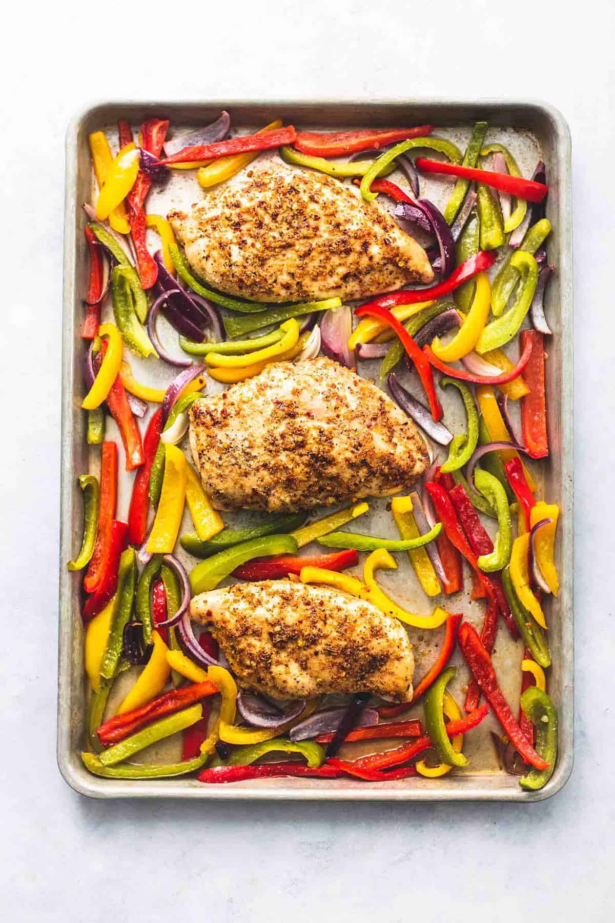 top view of chicken breasts and sliced peppers on a sheet pan.