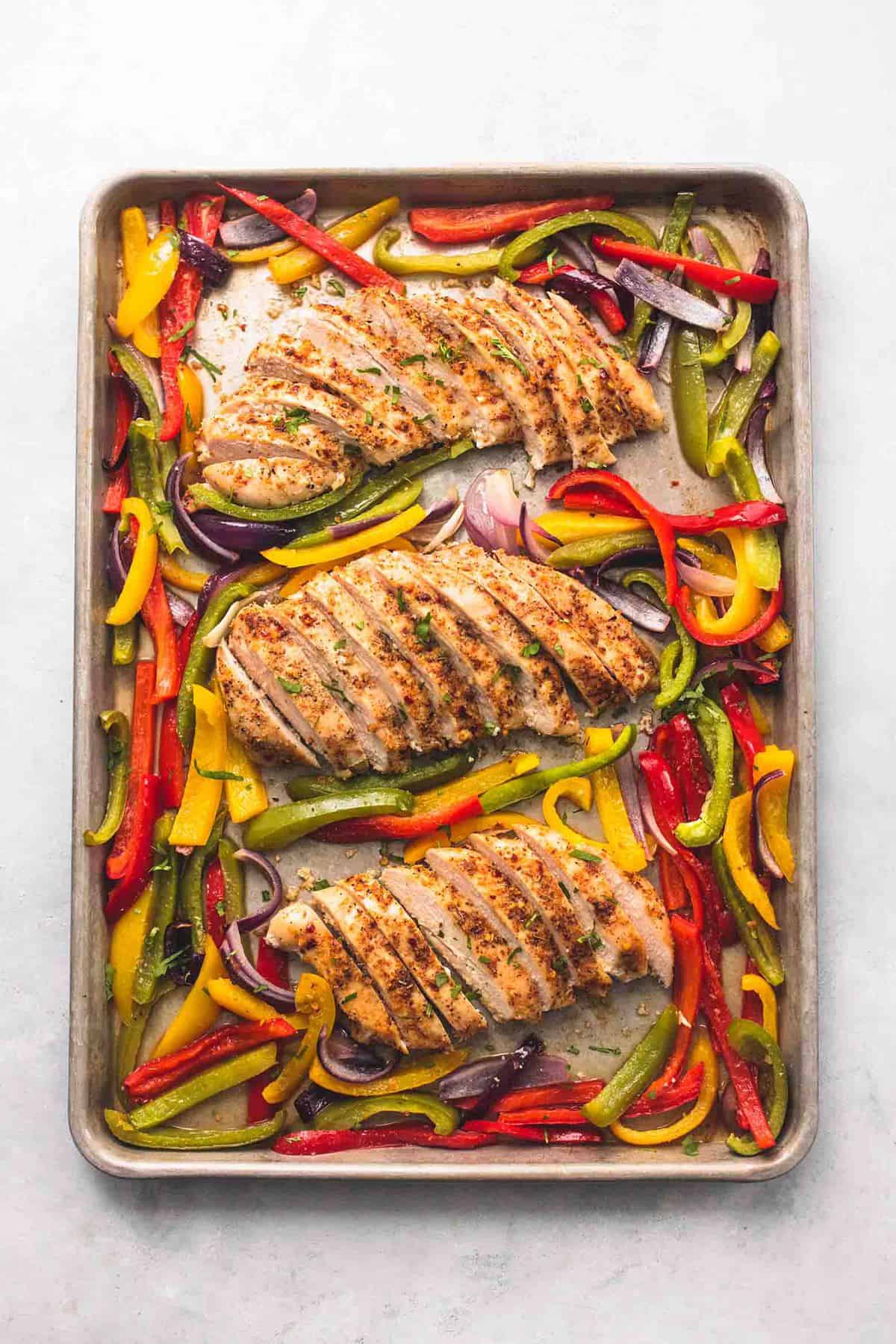 top view of sliced up chicken breasts and peppers on a sheet pan.