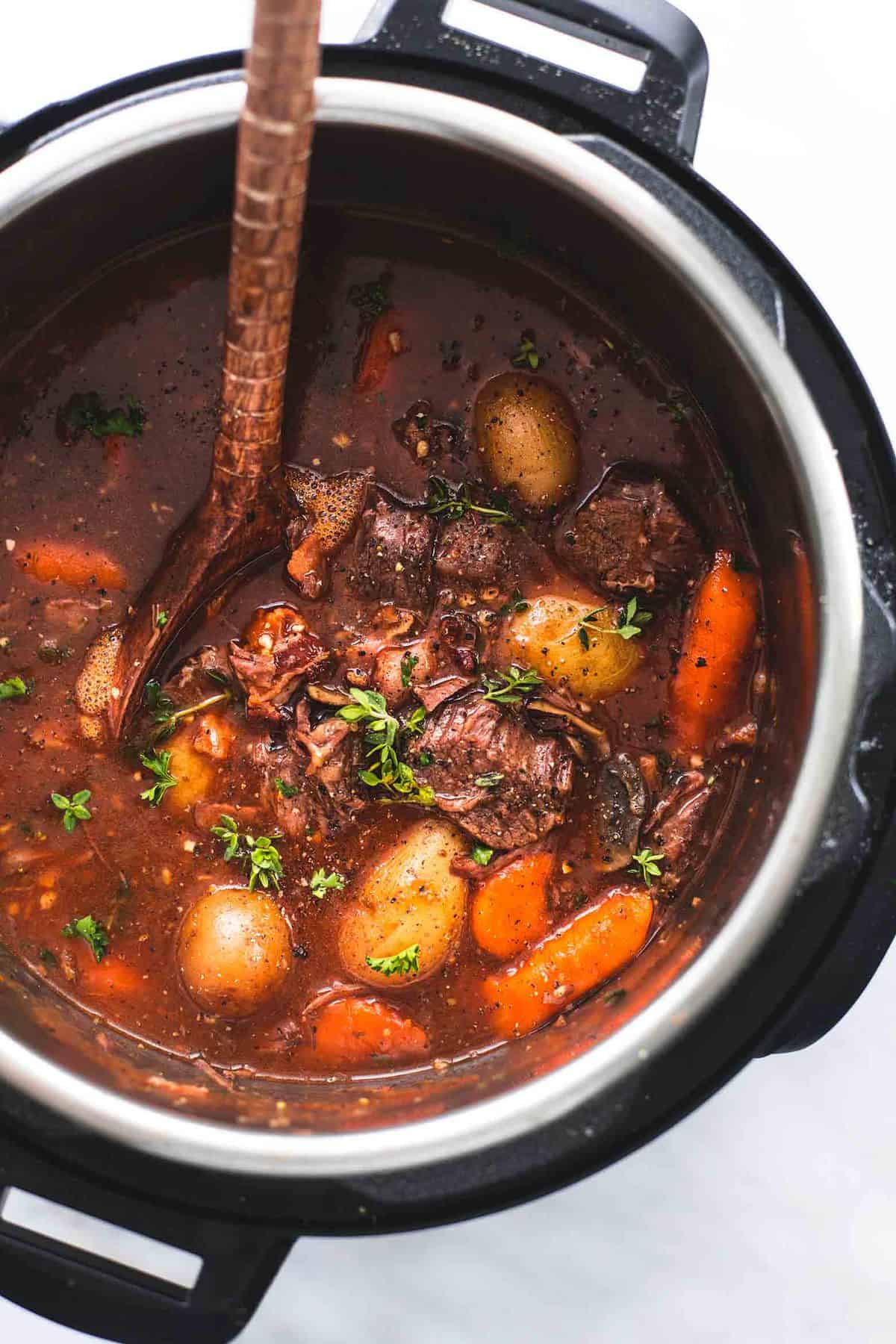 close up top view of instant pot beef bourguignon with a wooden serving spoon in an instant pot.