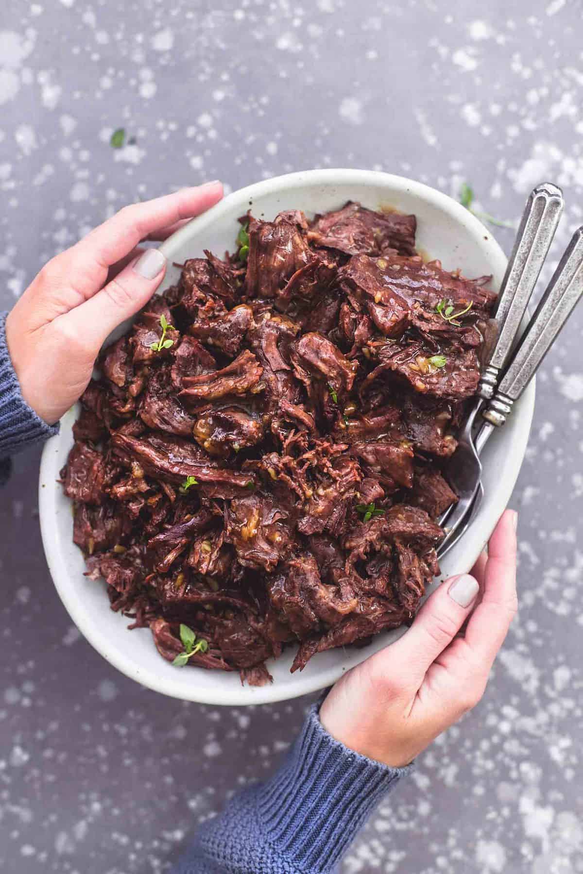 top view of a pair of hands holding a plate of instant pot pot roast with forks.