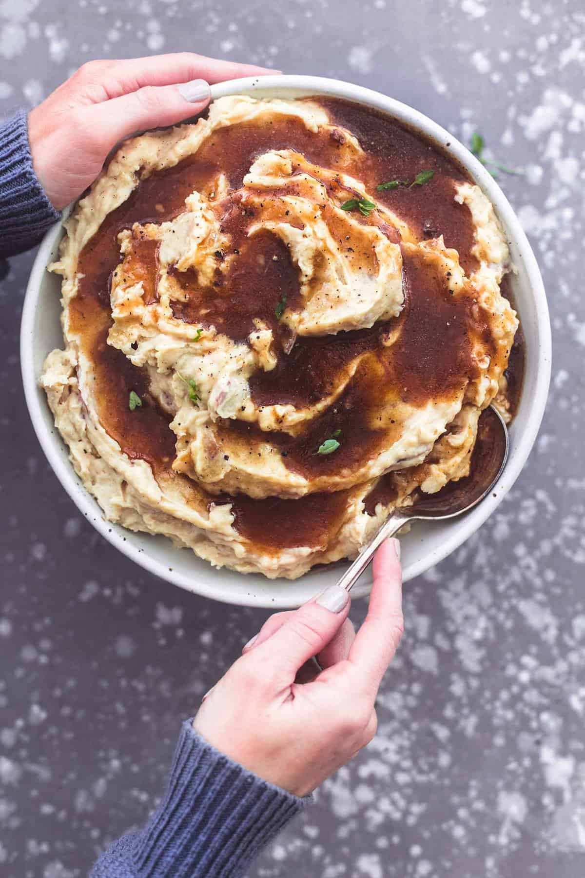 top view of one hand holding a bowl of mashed potatoes and the other scooping some up with a spoon.