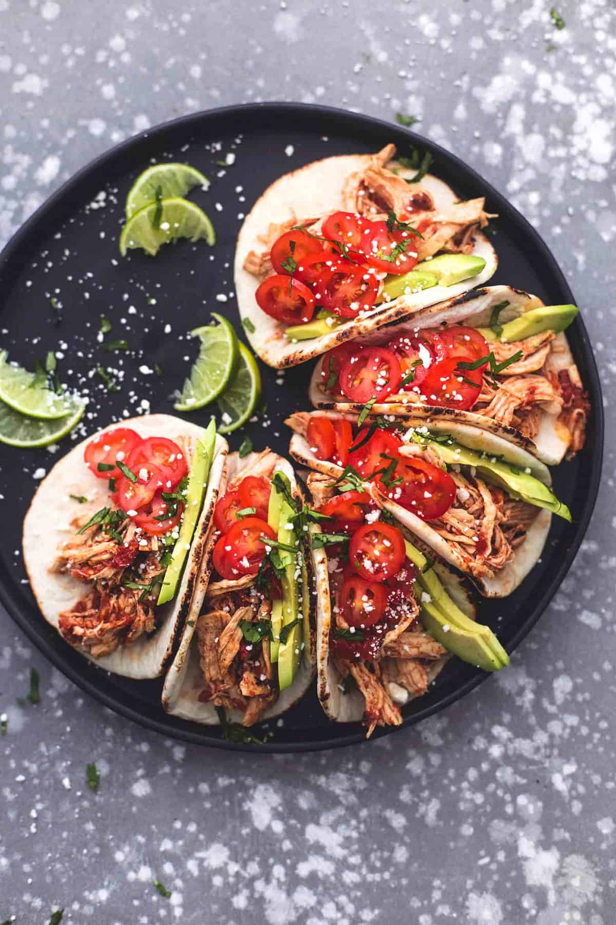 top view of instant pot shredded chicken tacos and lime slices on a round platter.