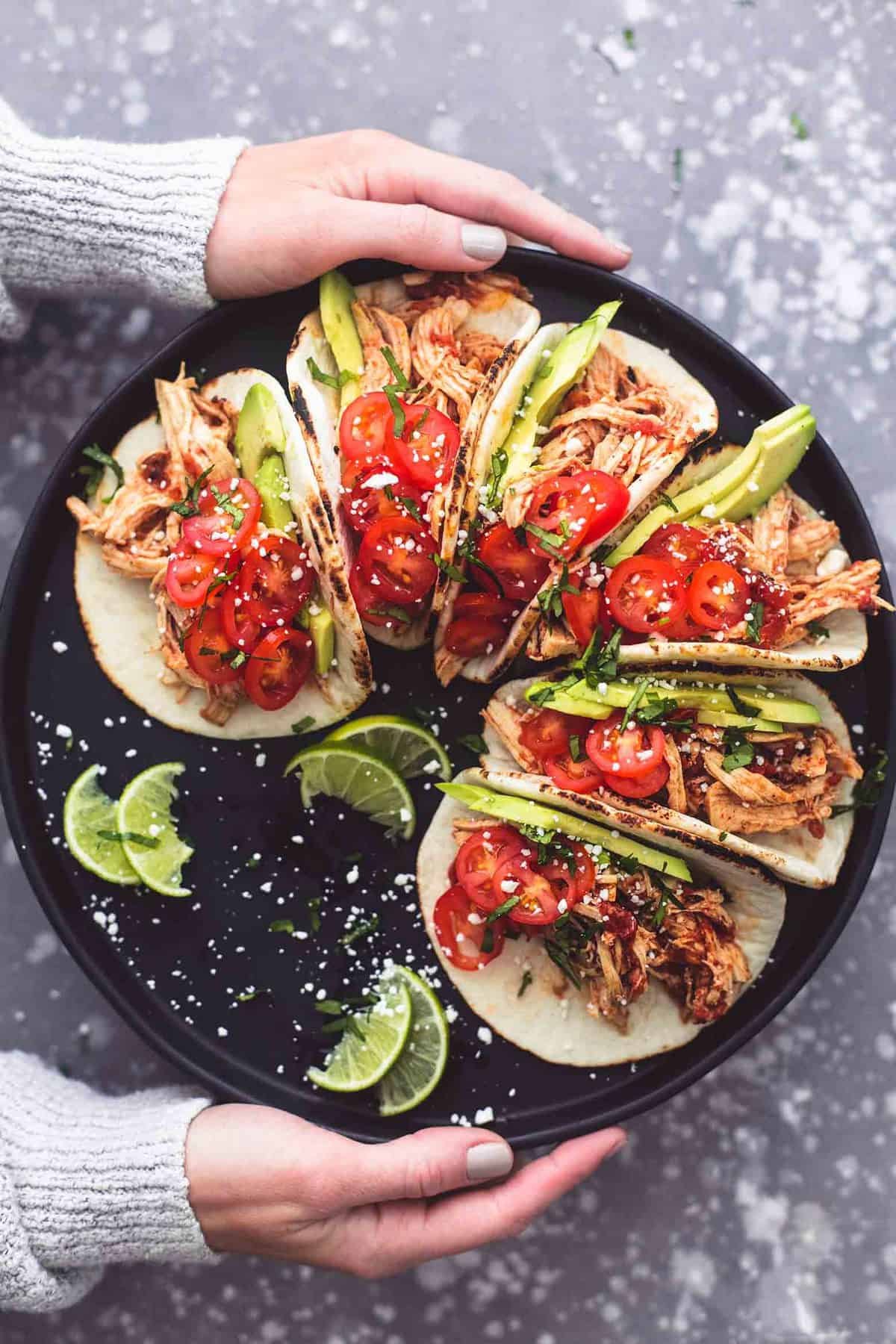 top view of a pair of hands holding a round platter with lime slices and instant pot shredded chicken tacos.