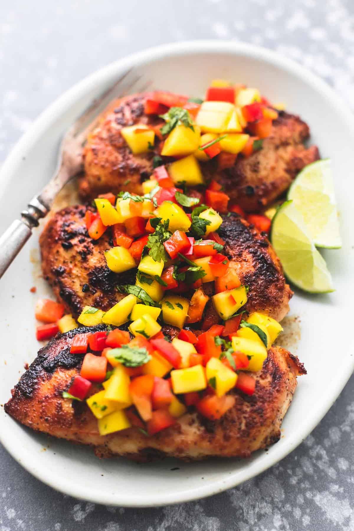 mango salsa chicken, lime slices and a fork on a plate.