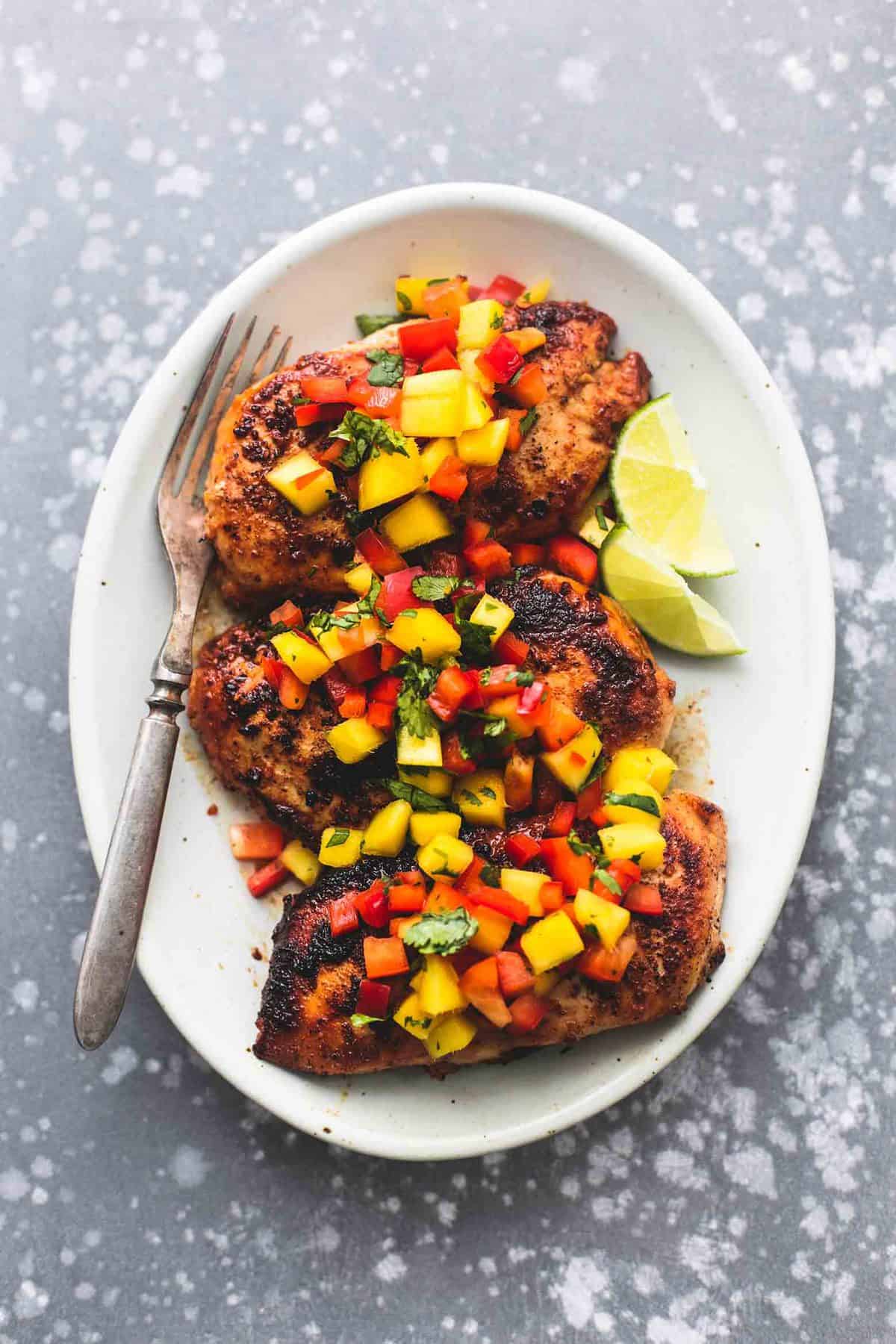 top view of mango salsa chicken, lime slices and a fork on a plate.