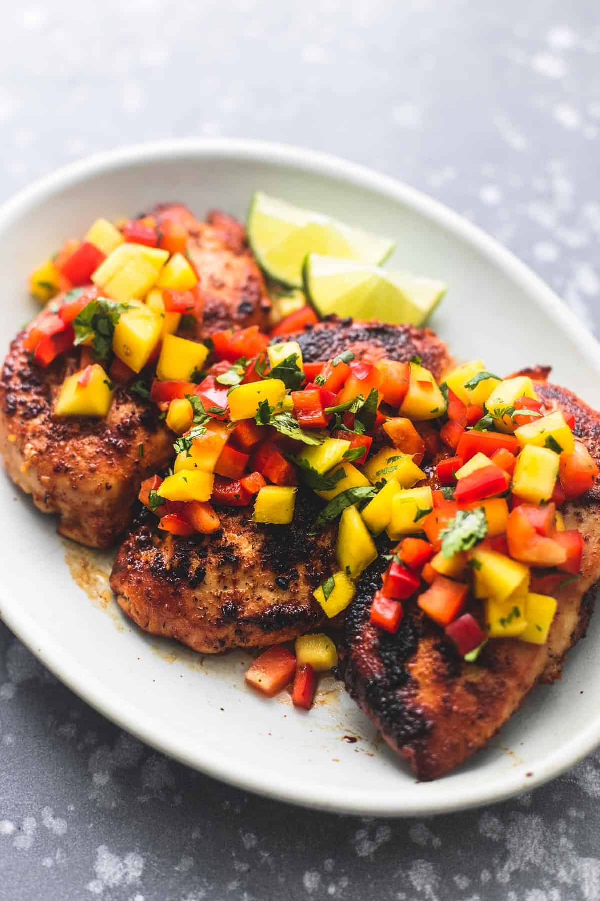 mango salsa chicken with lime slices on the side on a plate.