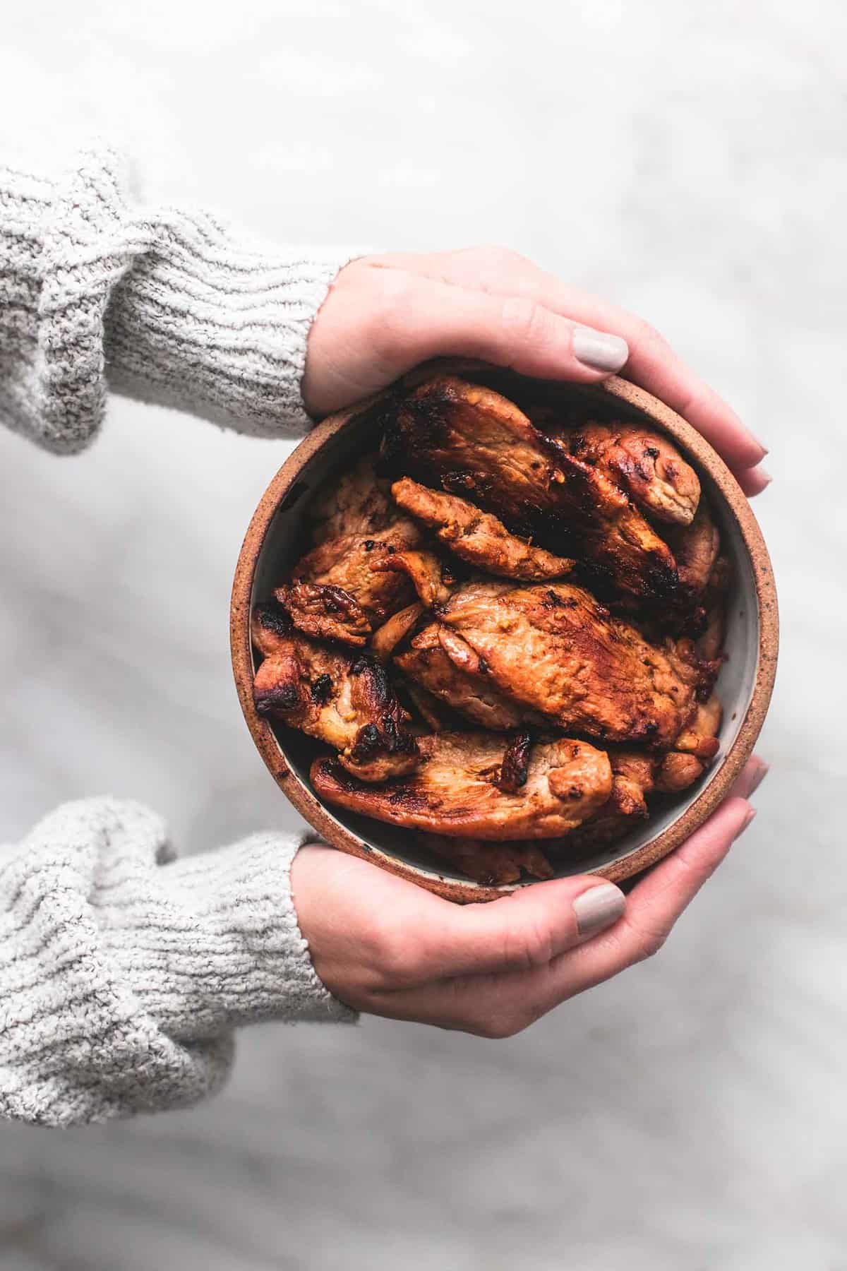 top view of a pair of hands holding a bowl of pork.