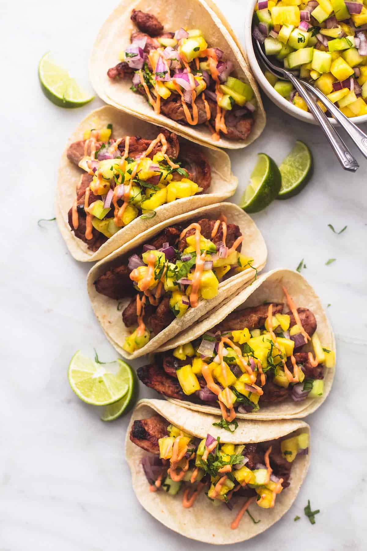 top view of pork tacos with pineapple salsa with lime slices and a bowl of more salsa on the side.