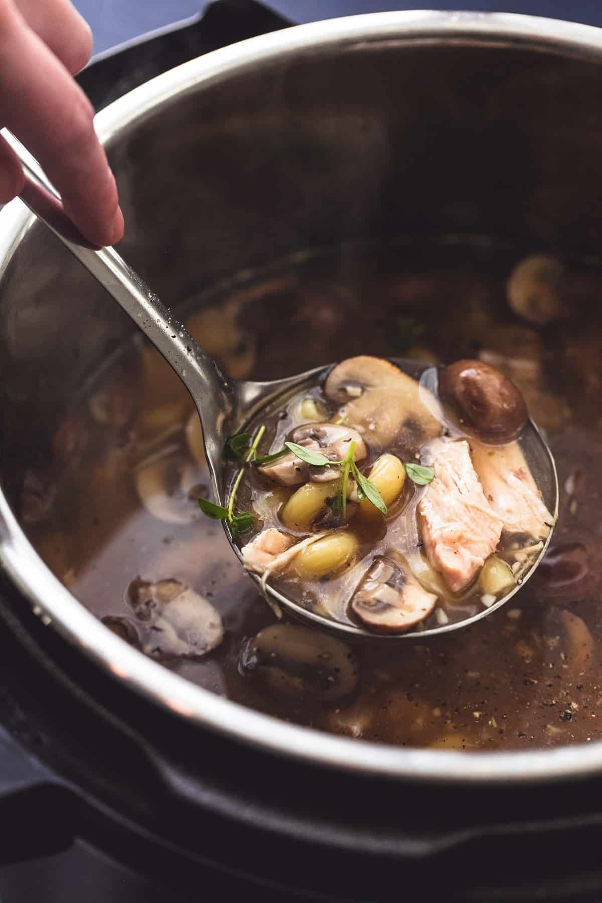 a hand lifting chicken marsala soup from an instant pot with a serving spoon.