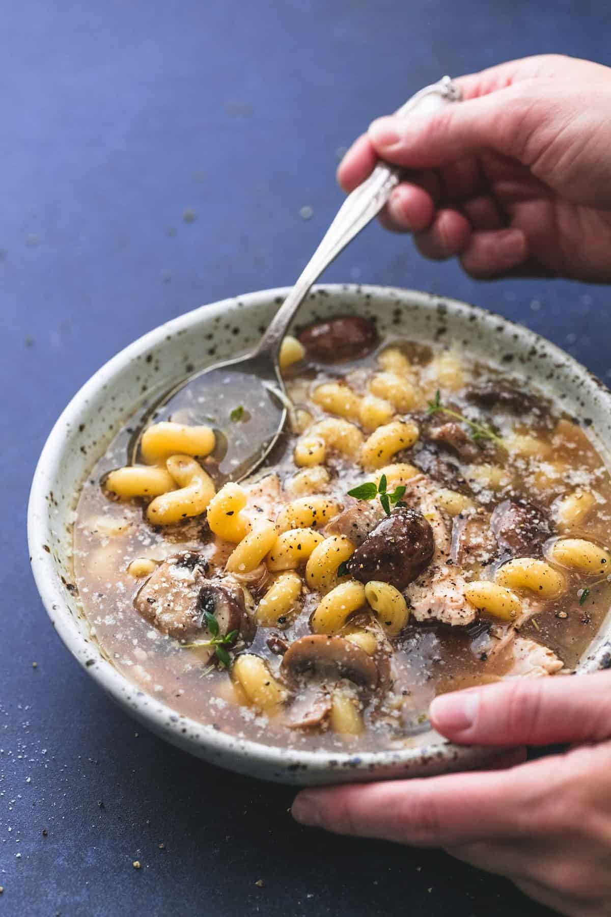 a hand scooping some chicken marsala soup with a spoon from a bowl.