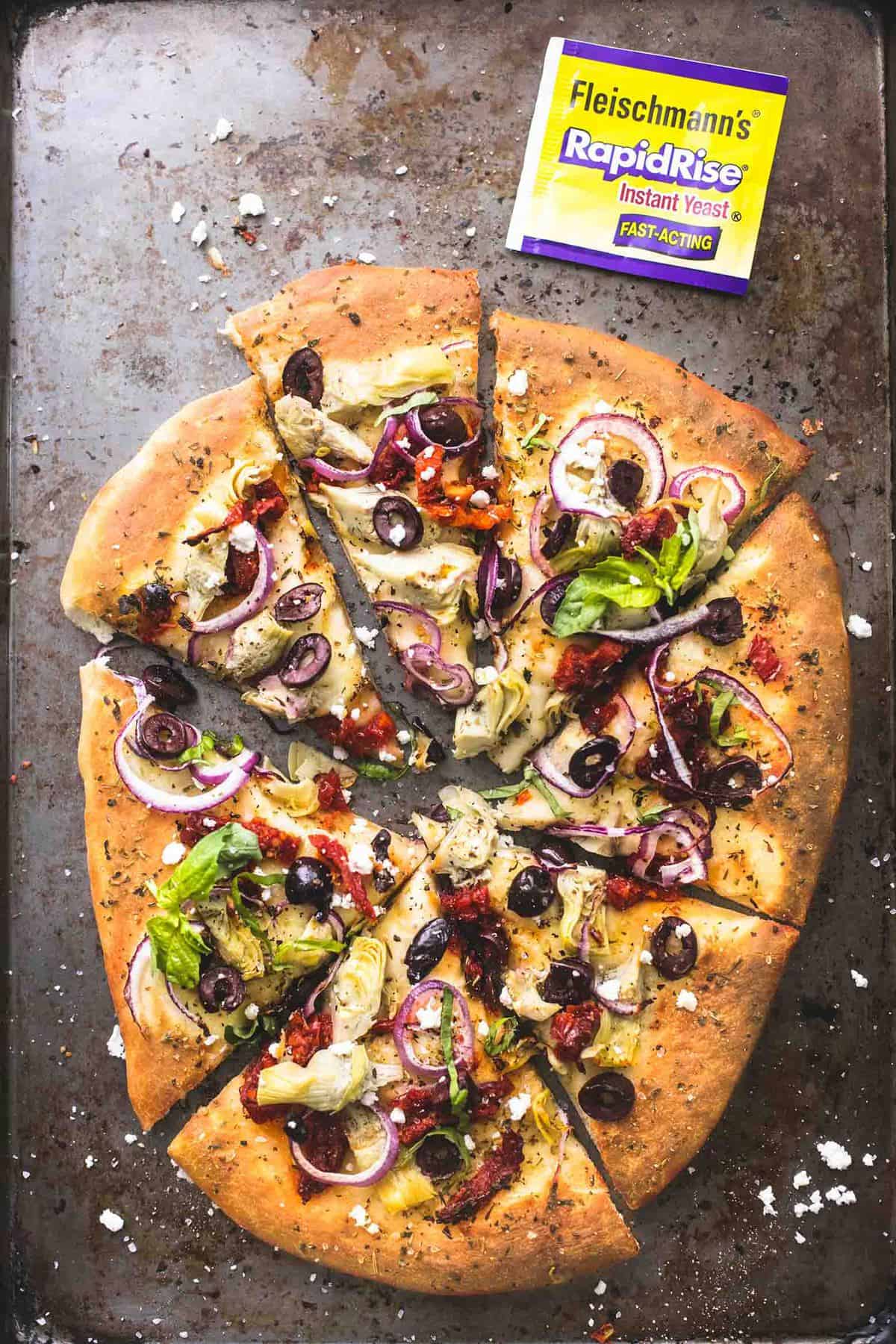 top view of Mediterranean veggie pizza cut up in slices with a RapidRise yeast packet on the side.