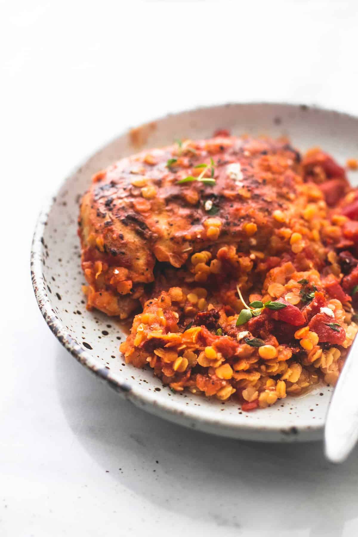 Greek sun dried tomato chicken and lentils with a fork on a plate.