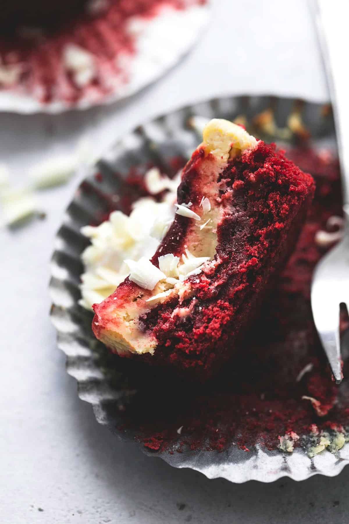 a red velvet cheesecake bite on an open cupcake liner missing a bite with a fork on the side.