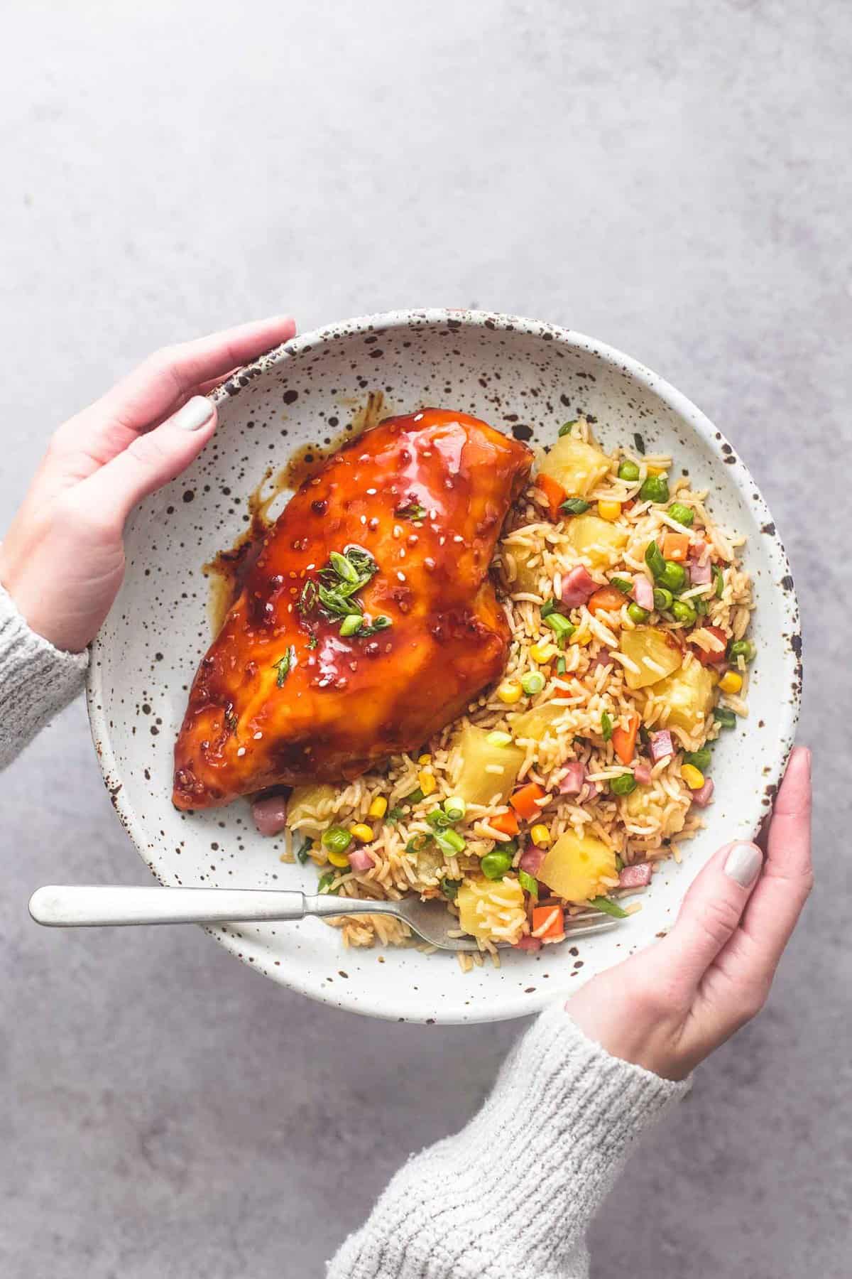 hands holding a plate with a fork and sheet pan teriyaki chicken and pineapple fried rice on it.