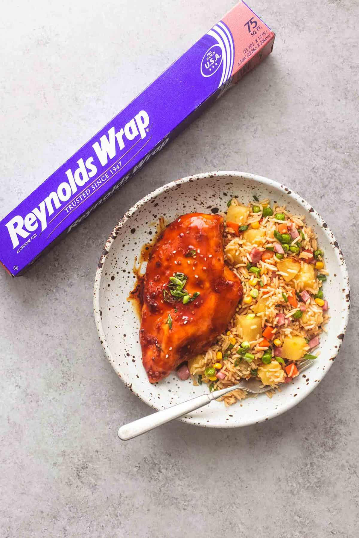 top view of sheet pan teriyaki chicken and pineapple fried rice with a fork on a plate with a foil wrap package on the side.