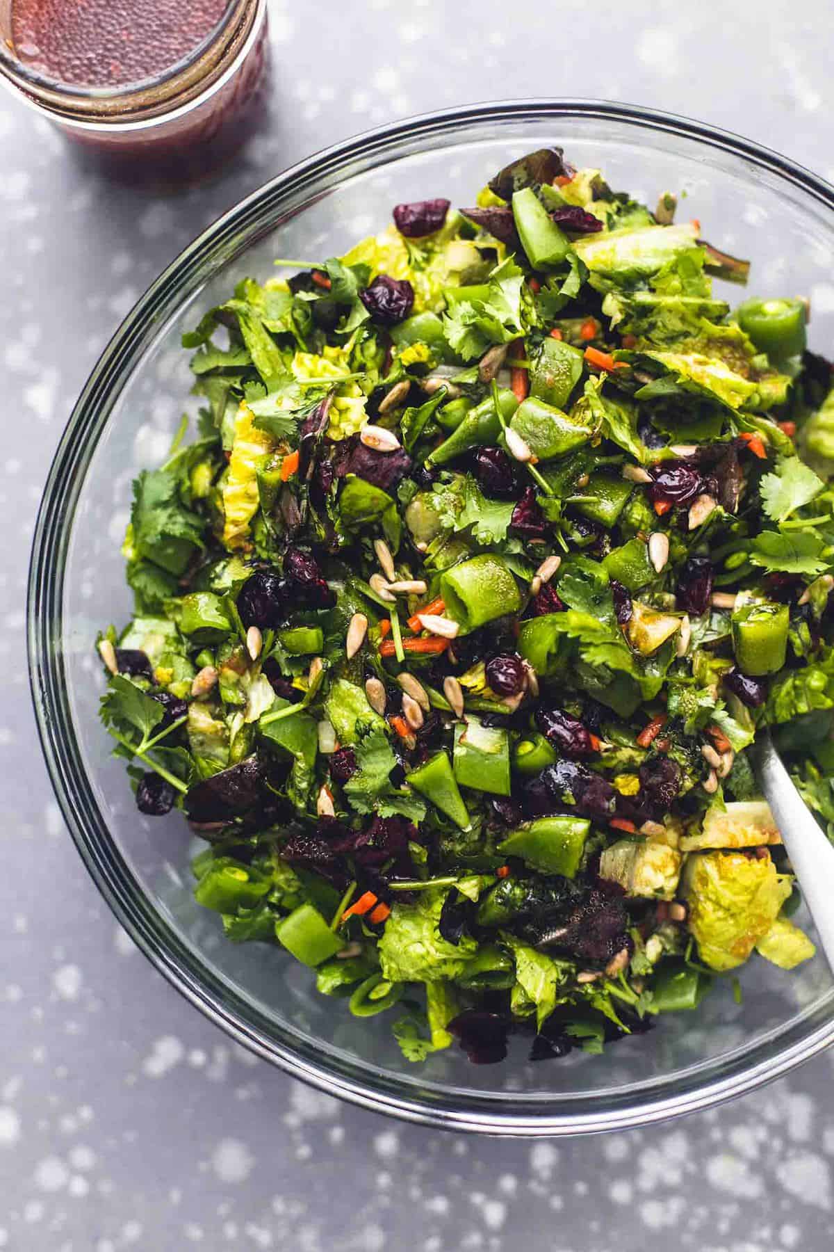 top view of chopped Asian salad with a serving spoon in a glass bowl with a jar of teriyaki dressing on the side.