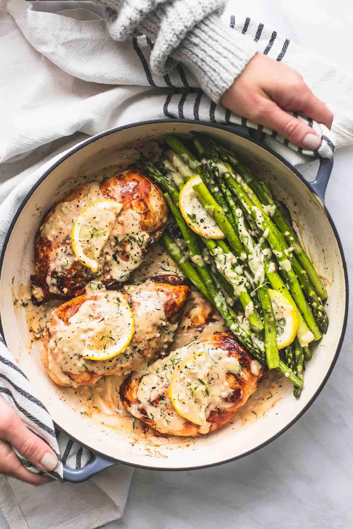 top view of hands holding a pan with creamy lemon chicken and asparagus in it.