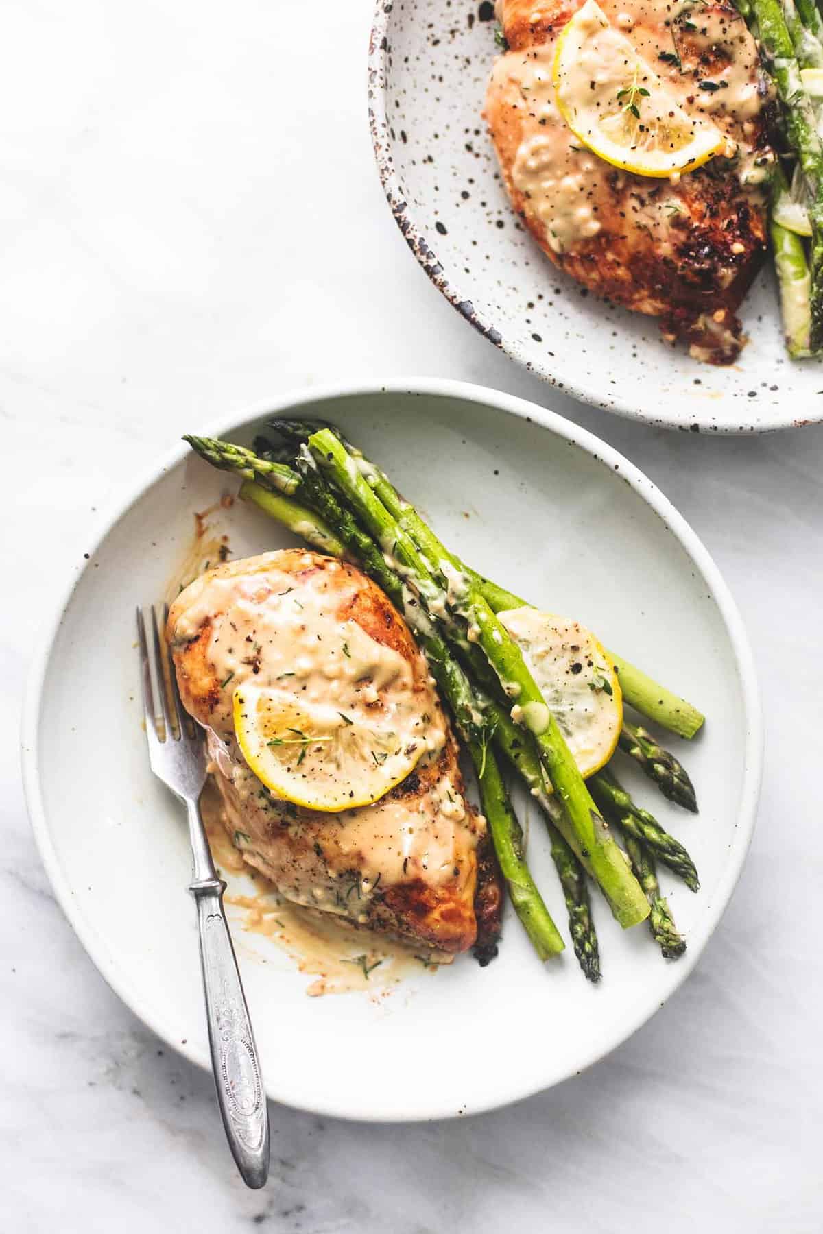 top view of creamy lemon chicken and asparagus with a fork on a plate with another plate full on the side.