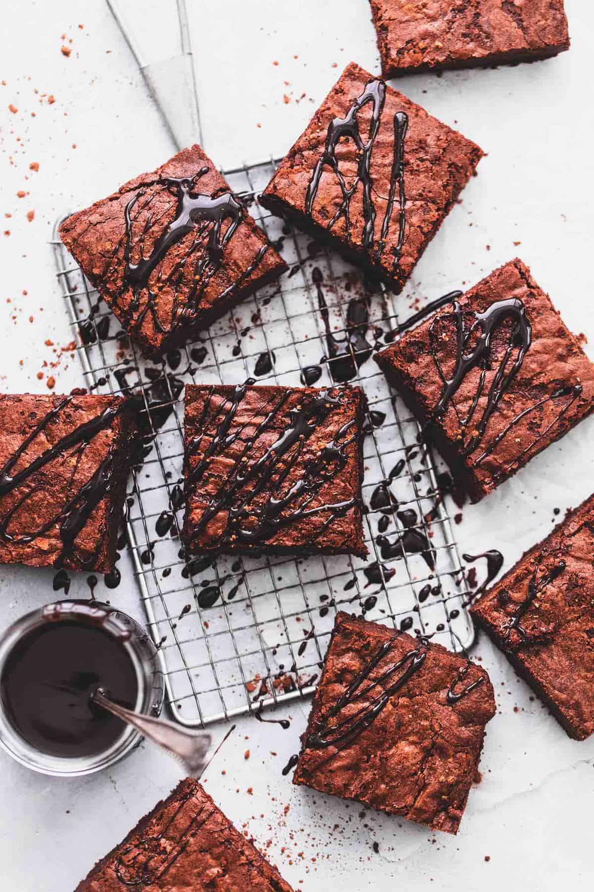 top view of brownies on and around a cooling rack with hot fudge drizzled on top with a jar of hot fudge with a spoon on the side.