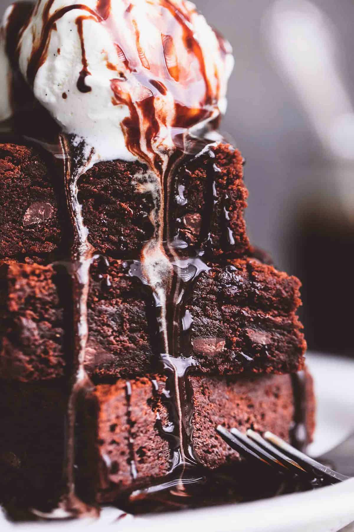 close up of stacked brownies with a scoop of ice cream on the top with a fork on the side.