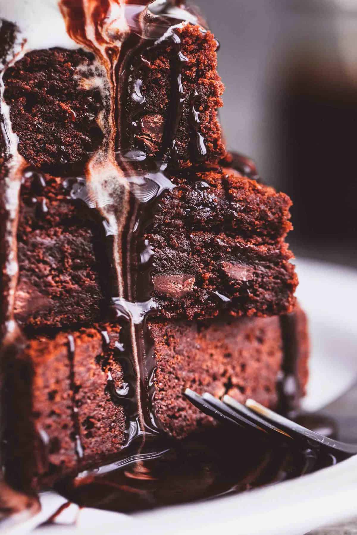 close up of a stack of brownies with hot fudge and ice cream on top and a fork on the side.