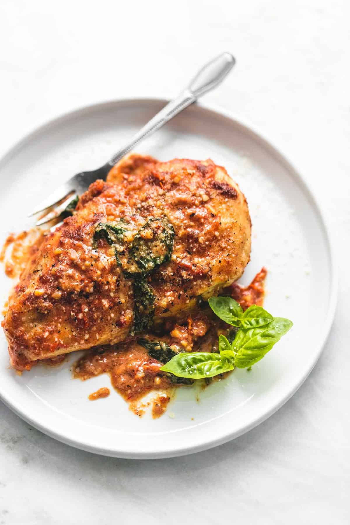 a piece of creamy Tuscan parmesan chicken with a fork on a plate.