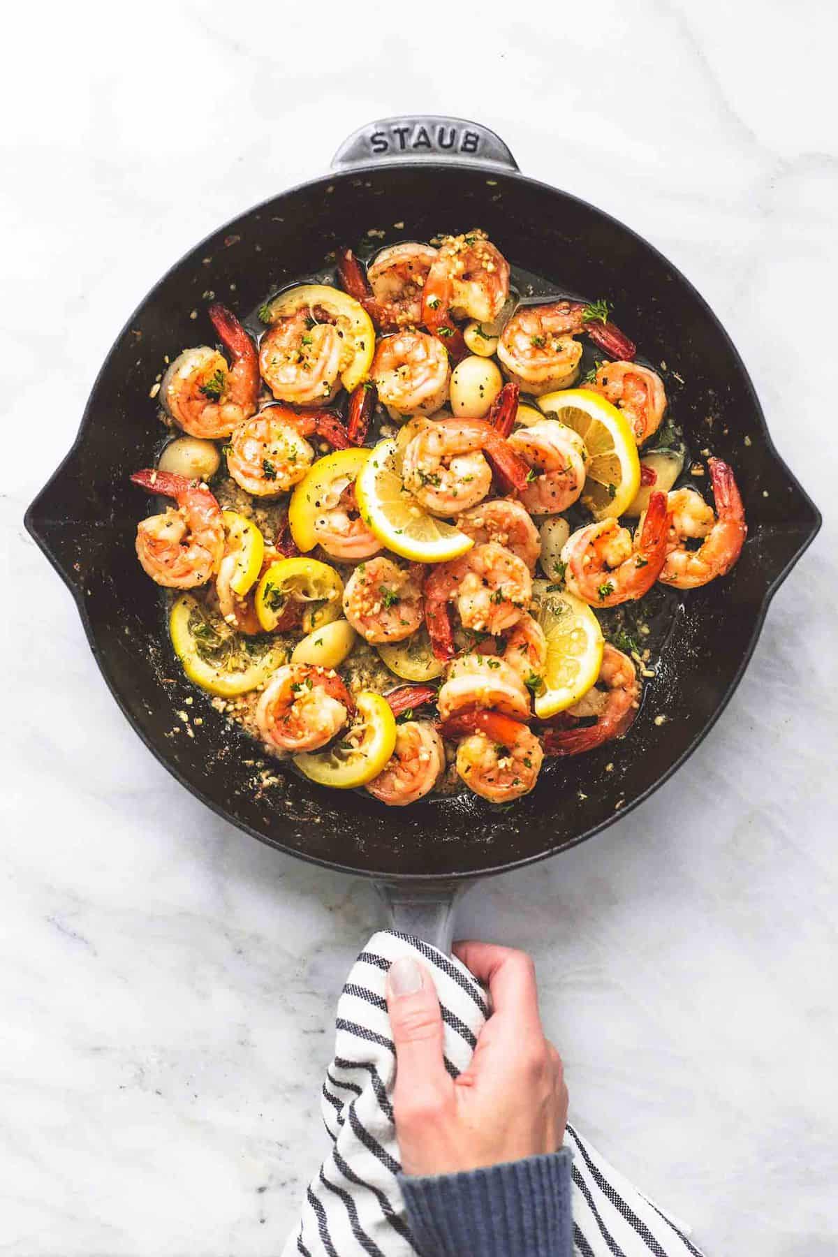 top view of lemon garlic butter shrimp in a pan with a hand holding the handle.