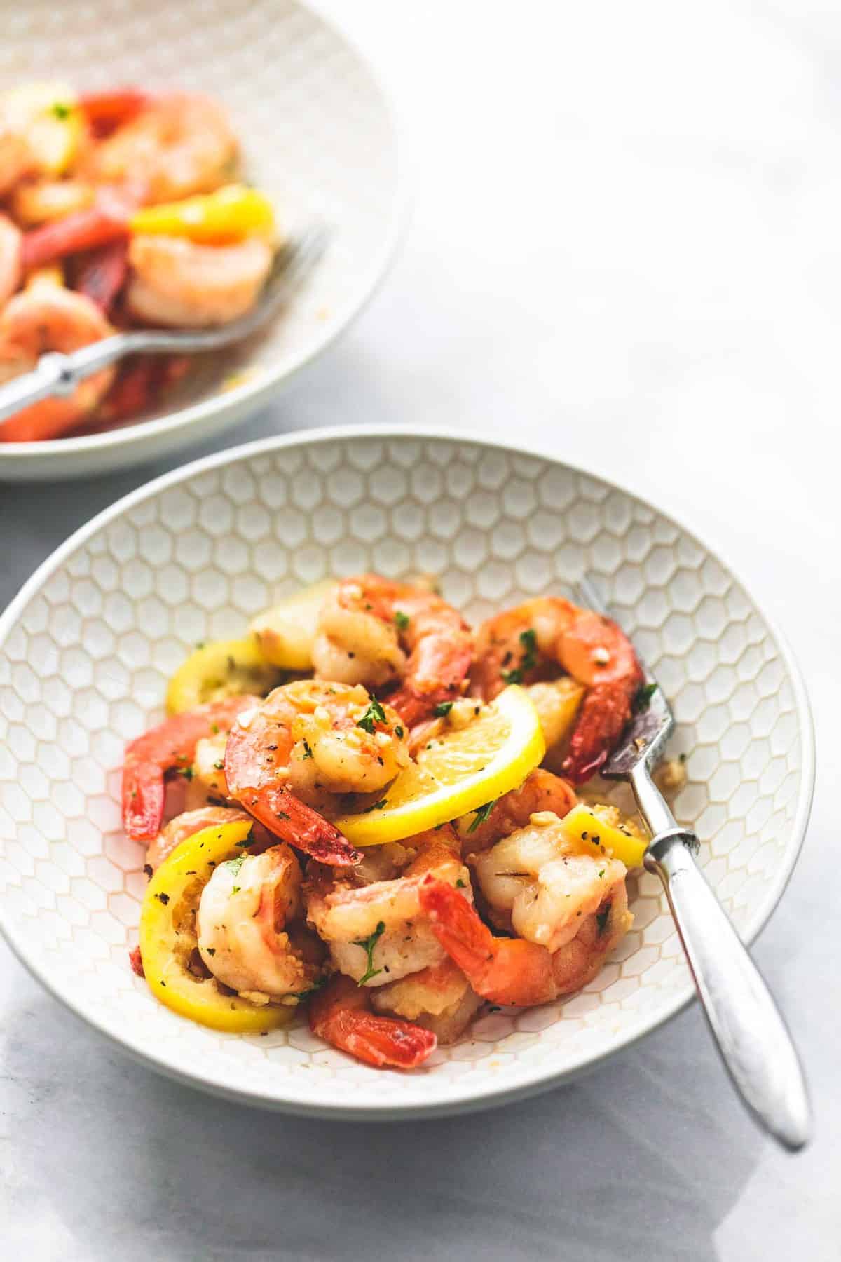 lemon garlic butter shrimp with a fork in a bowl with another bowl in the background.