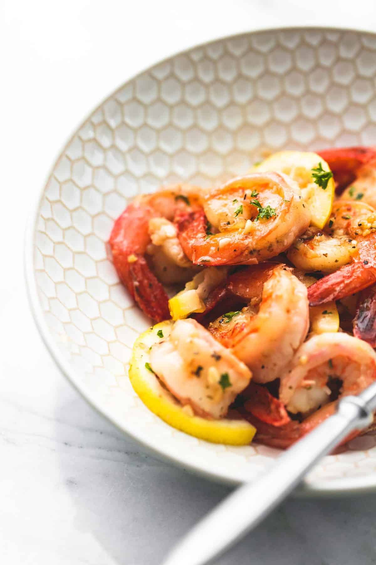 close up of lemon garlic butter shrimp with a fork in a bowl.