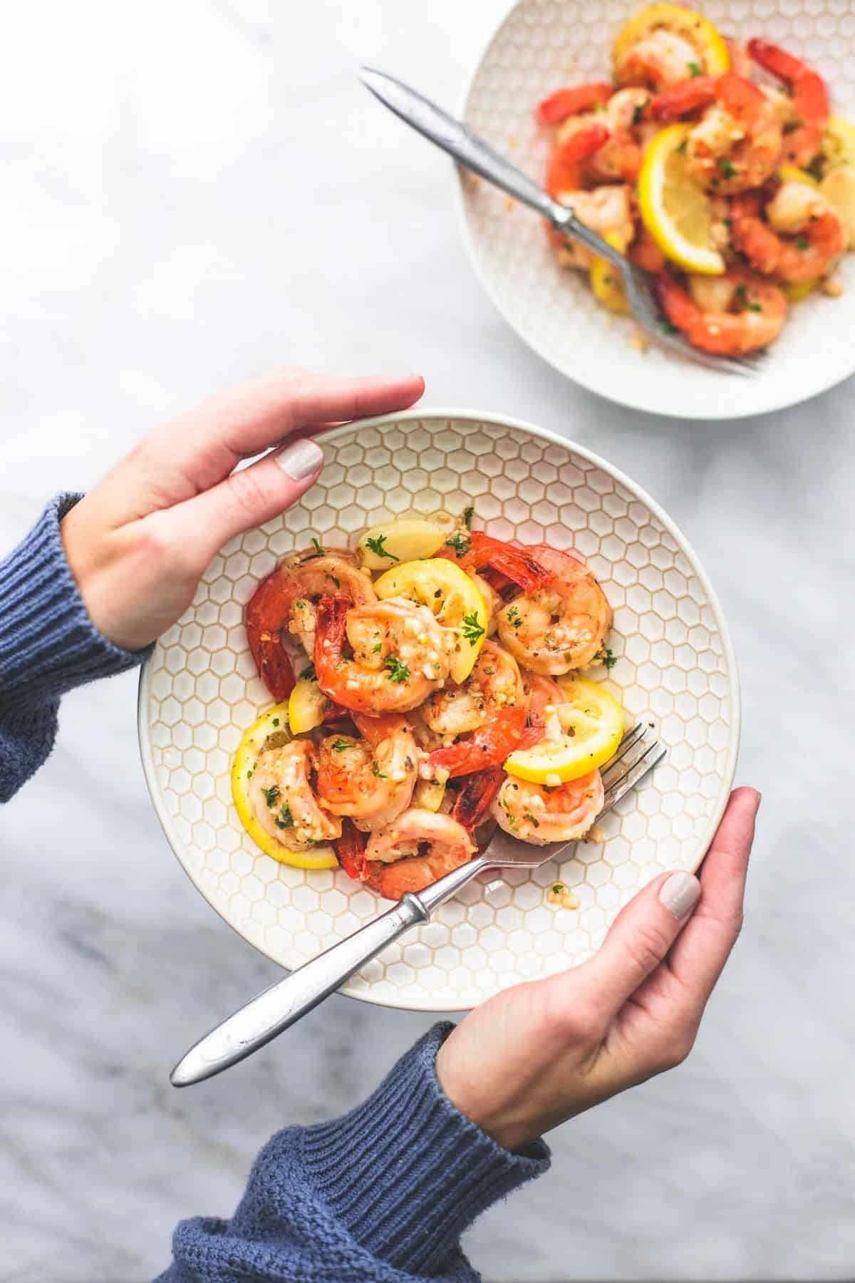 top view of hands holding up a bowl with a fork and lemon garlic butter shrimp in it with another bowl of shrimp on the side.