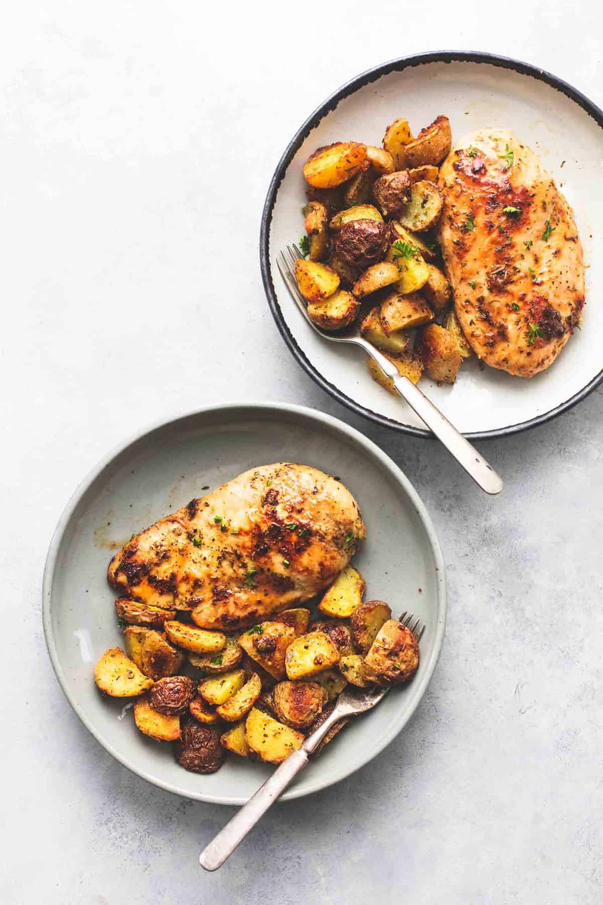 top view of two plates with sheet pan chicken and potatoes and forks on them.