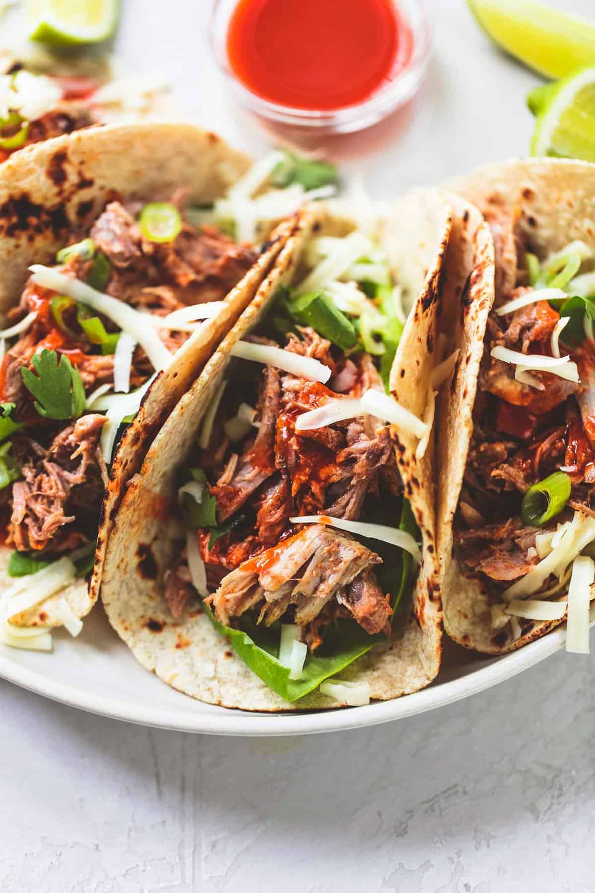 close up of slow cooker pork tacos with sauce on the side all on a plate.