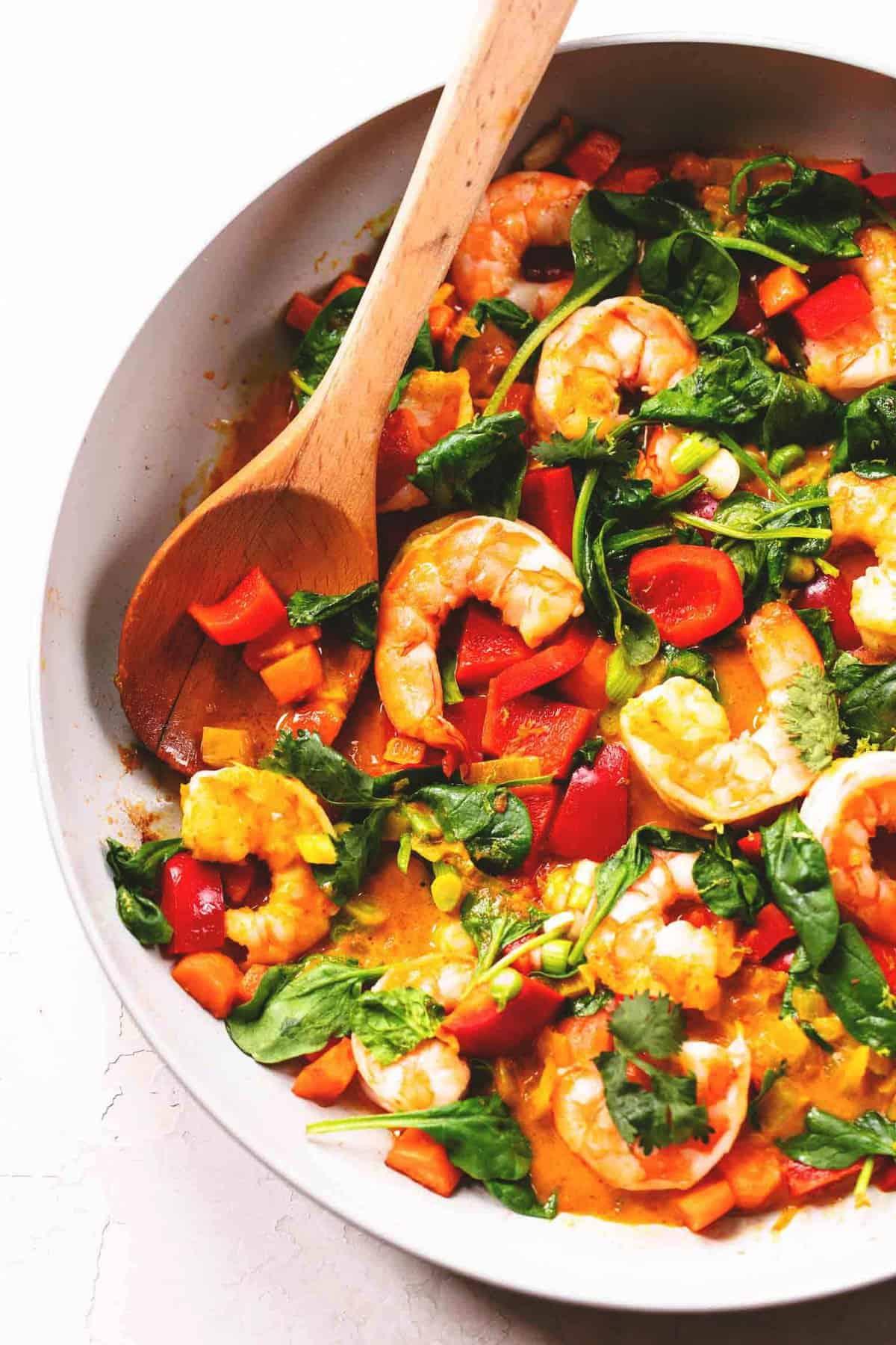 close up top view of Thai coconut curry with a wooden serving spoon in a pan.