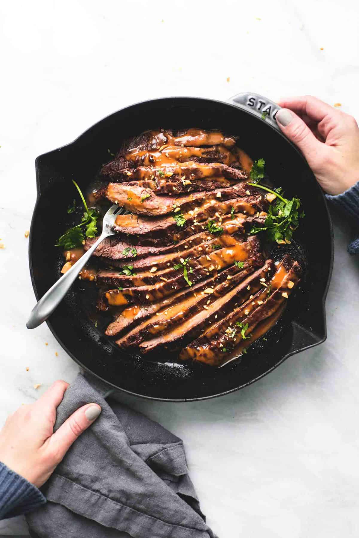 top view of Thai peanut beef with a fork in a pan with hands on the side and handle of the pan.