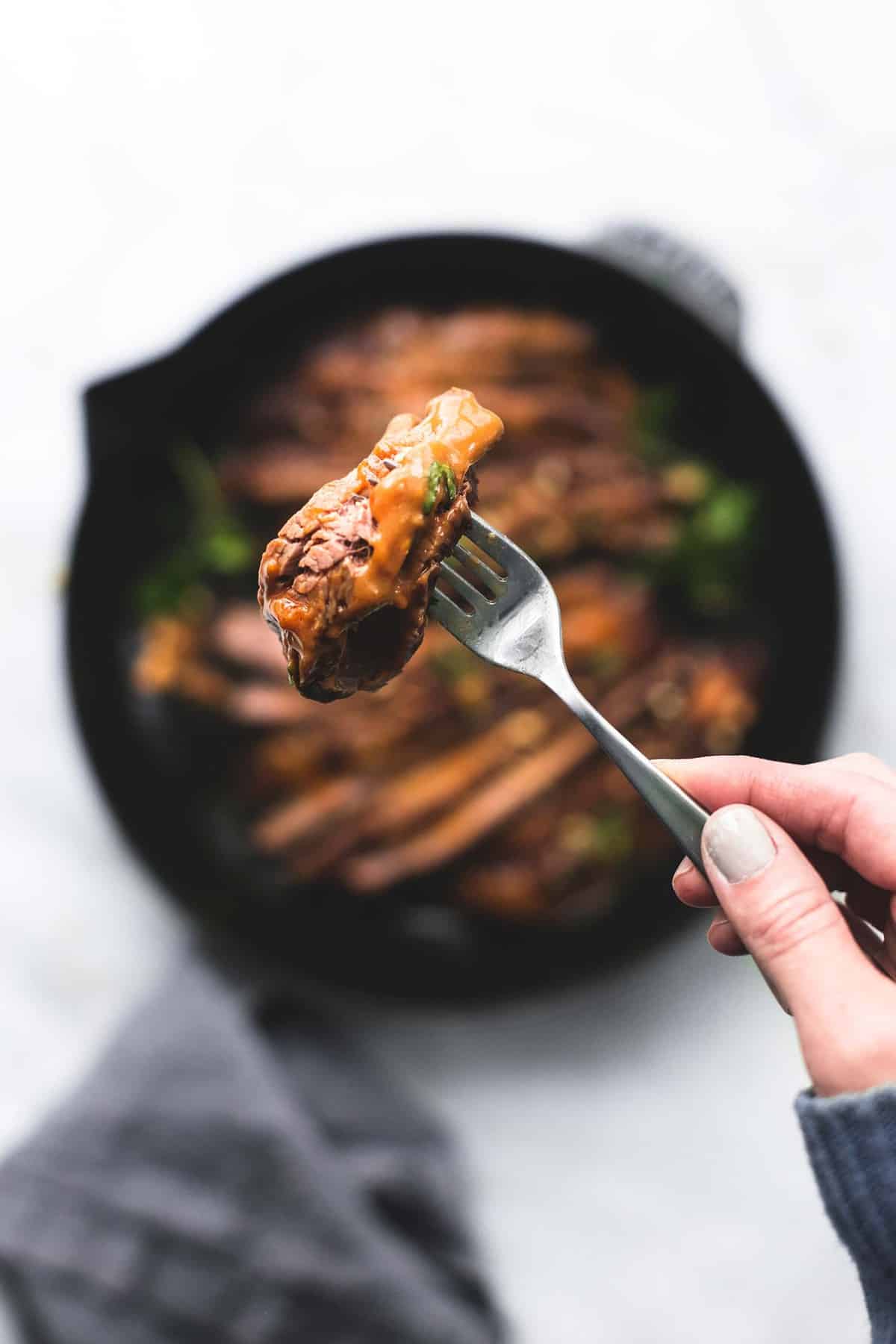 a hand holding up a fork with a piece of Thai peanut beef on it above a pan of more beef.