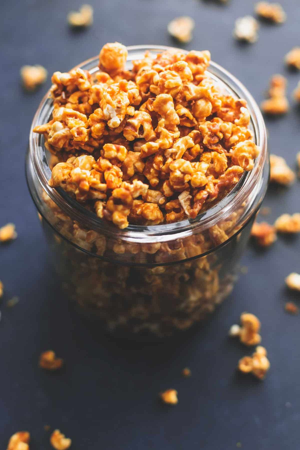 caramel corn in a tall glass jar with more caramel corn around it.