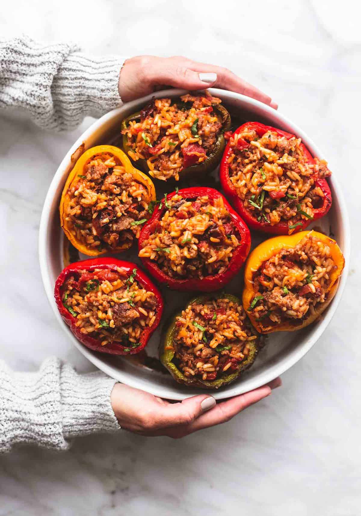 top view of hands holding a round dish of stuffed peppers.