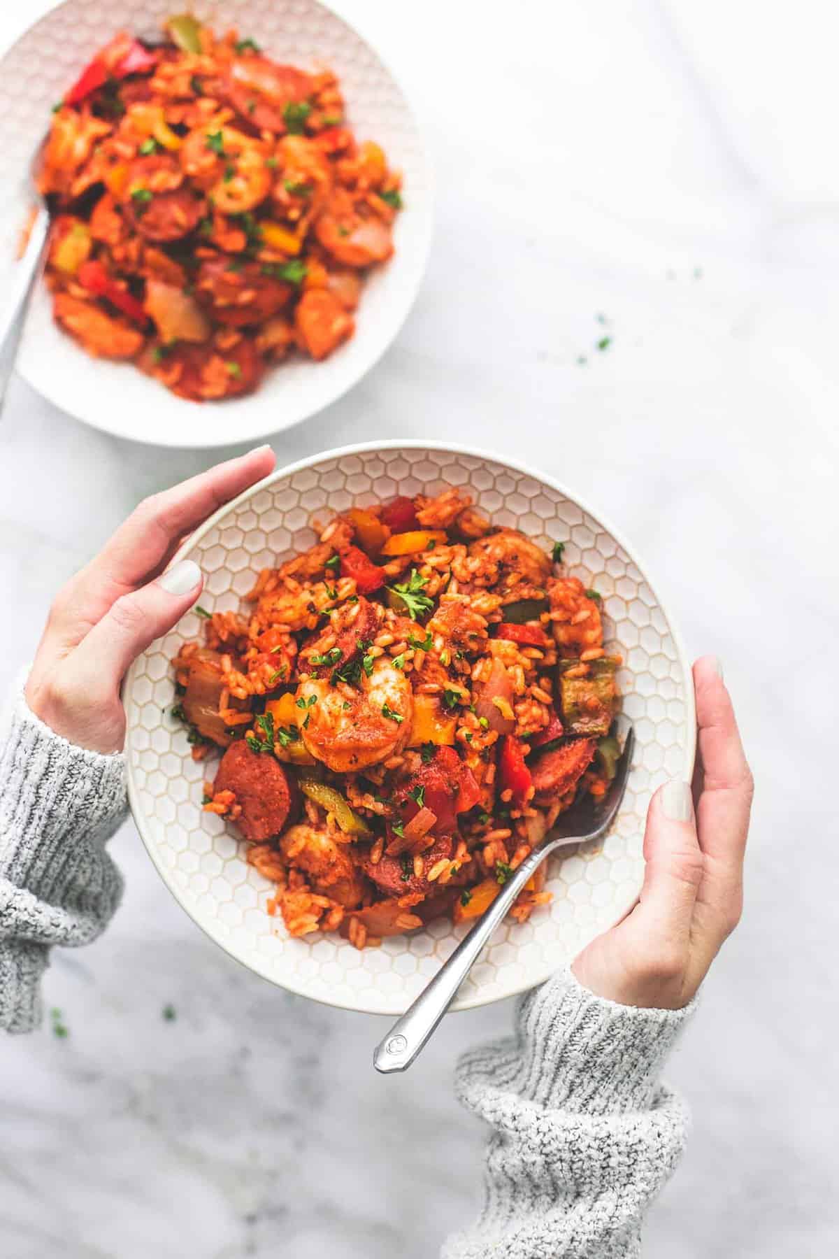 top view of hands holding up a bowl with a fork and sheet pan jambalaya in it with another bowl on the side.