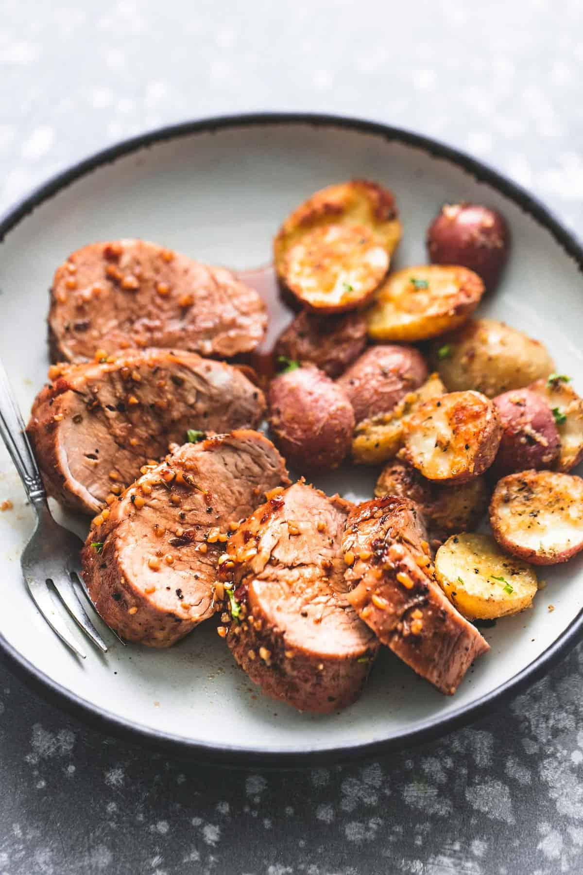 close up of sheet pan pork tenderloin and potatoes with a fork on a plate.