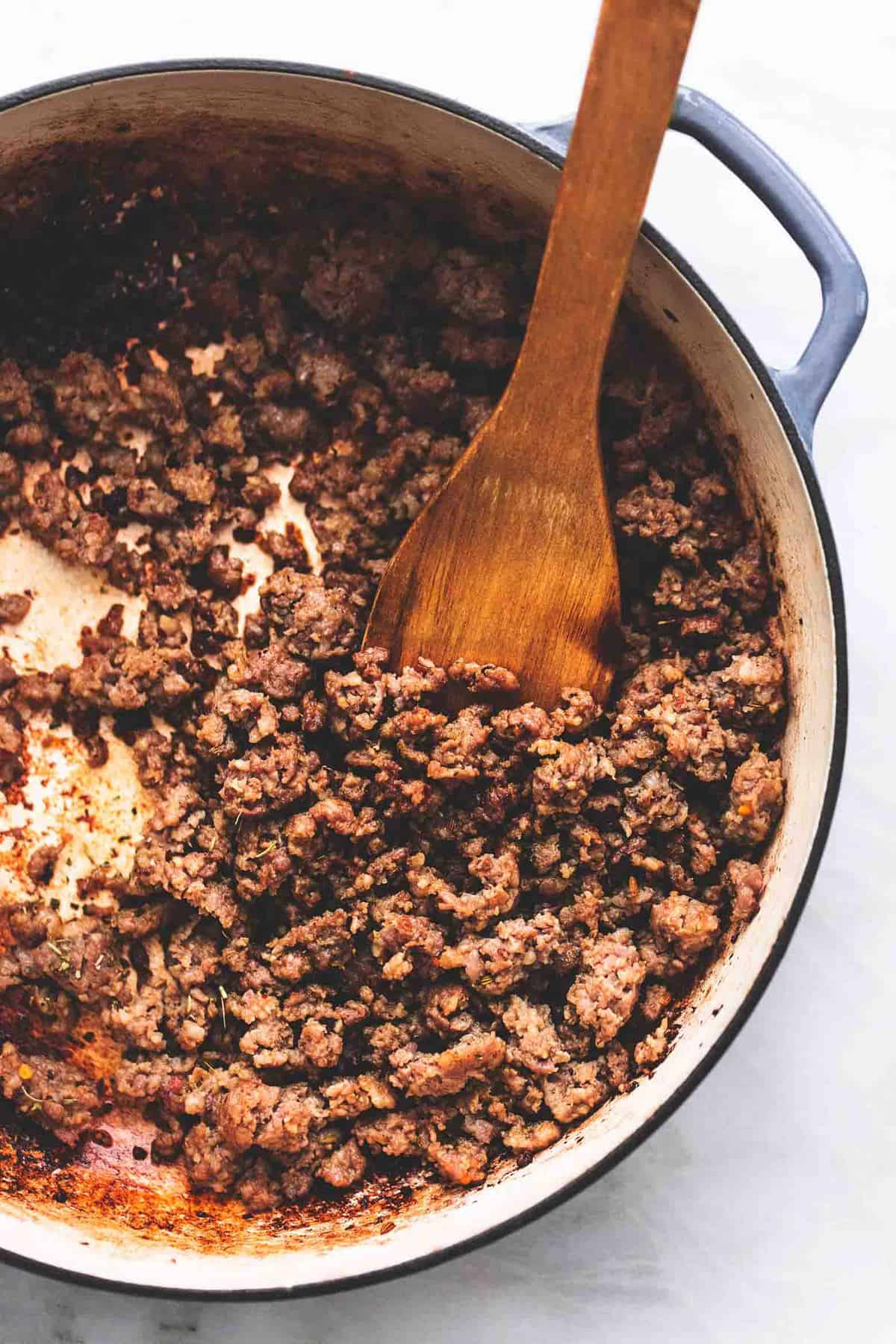 top view of ground beef cooked in a skillet with a wooden spatula.