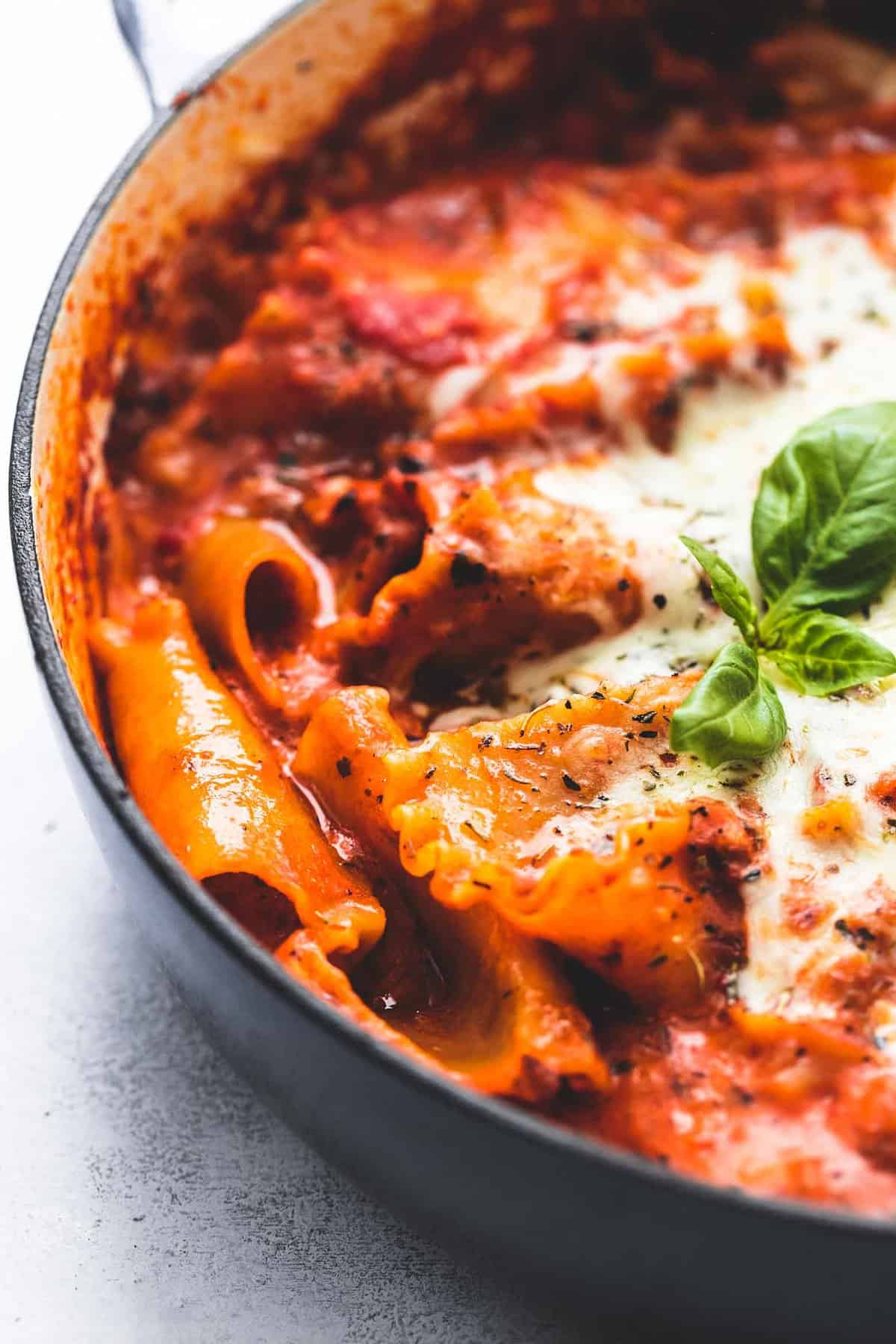 close up of cooked lasagna noodles in red sauce with fresh basil in a skillet.