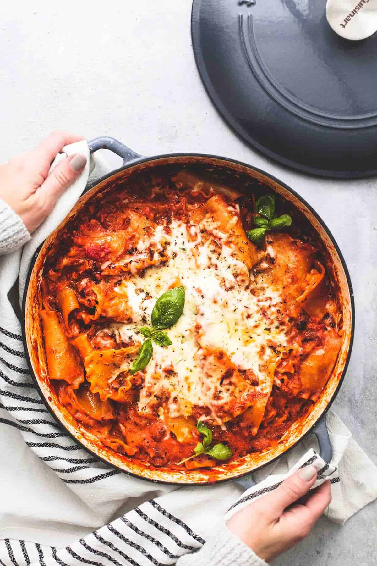 top view of one pot lasagna in a pot with a pair of hands holding the handles on the side.