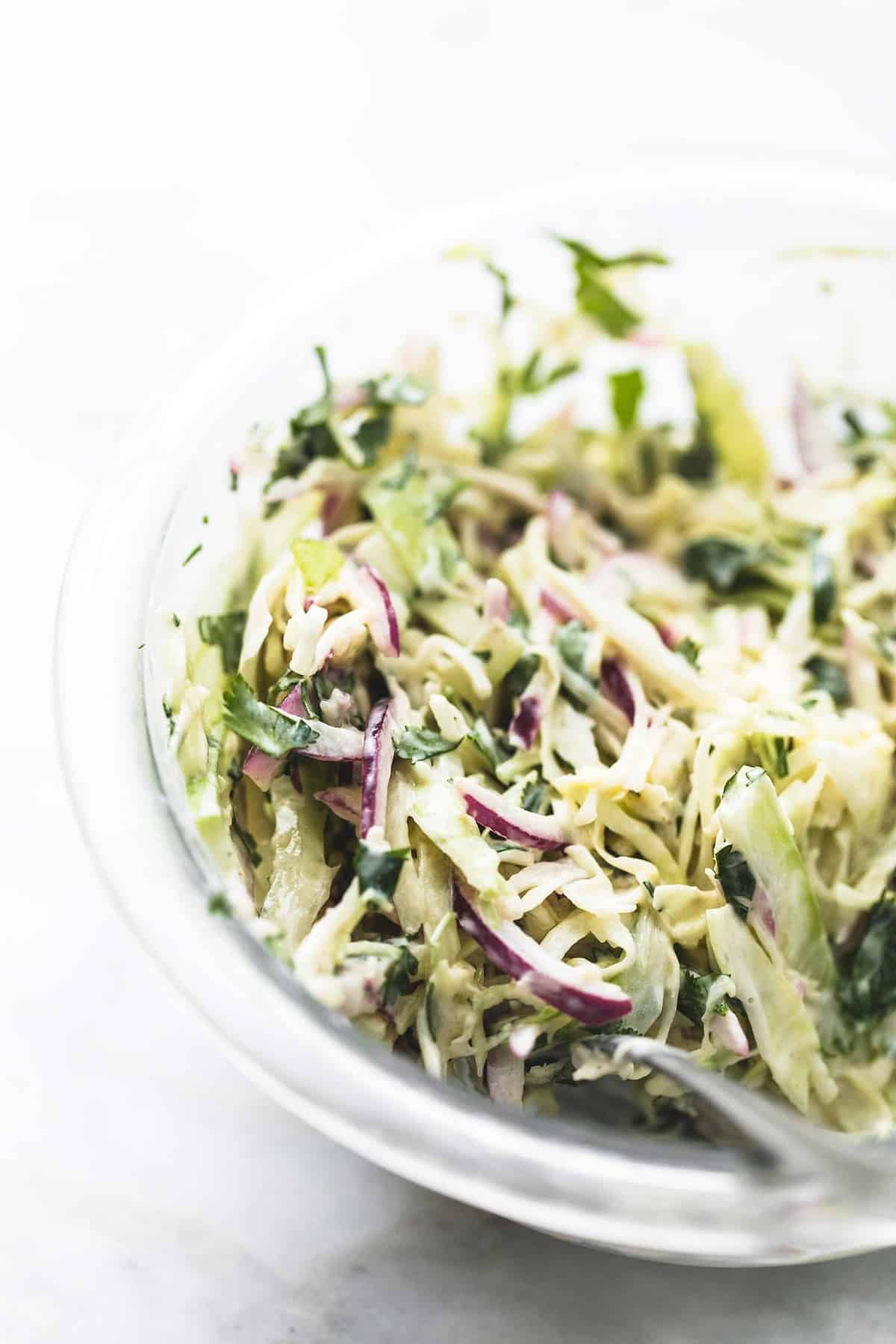 close up of cole slaw with a spoon in a glass bowl.