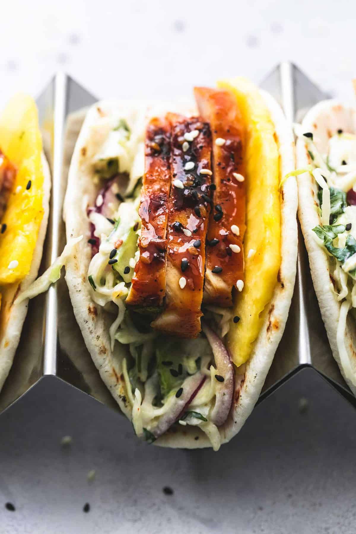 close up of a teriyaki chicken taco in a taco holder with more tacos on the side.